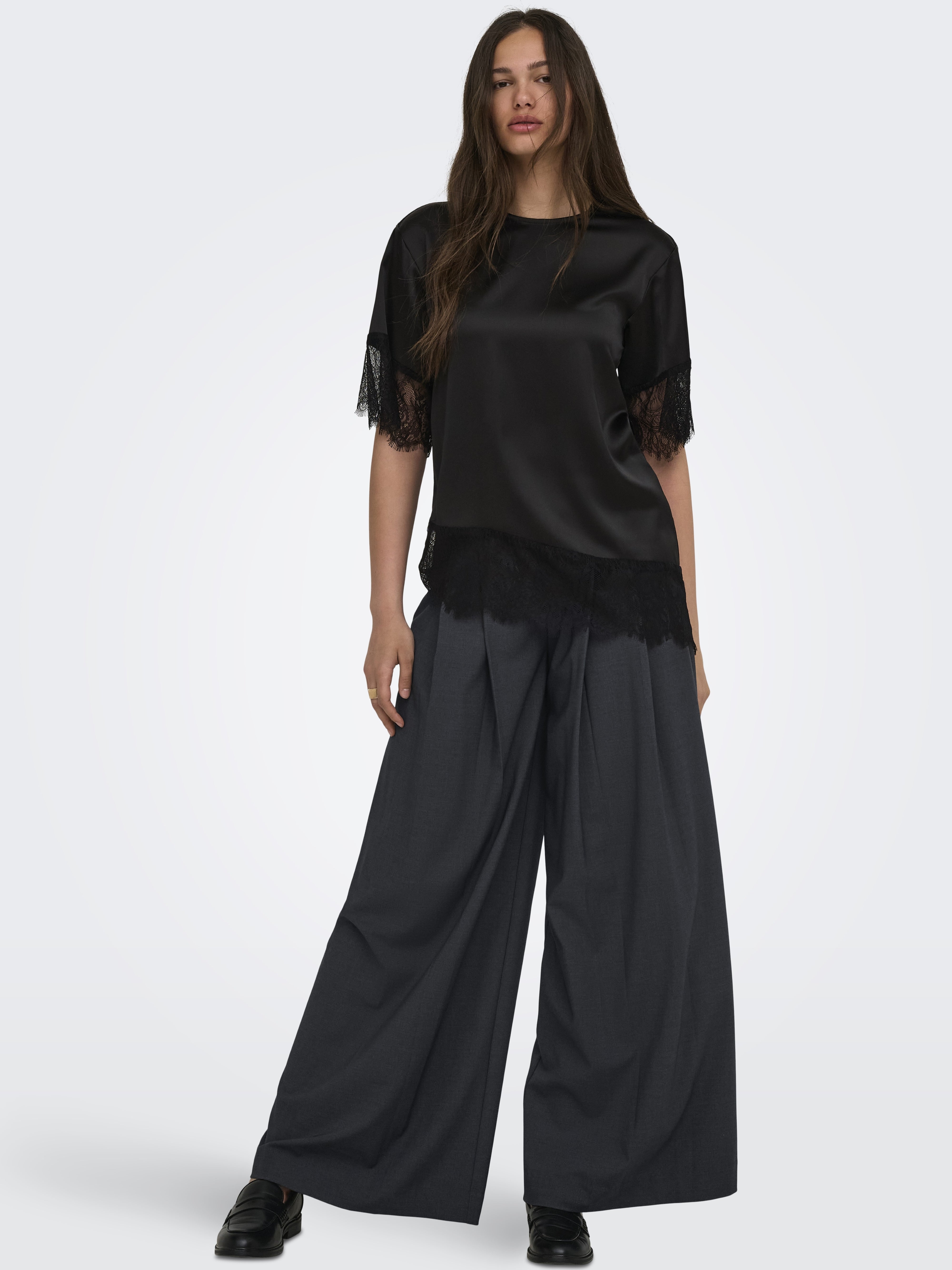 Black satin short-sleeve top with lace trim paired with wide-leg dark gray trousers and black shoes.