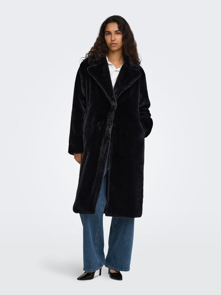 Black plush coat over a white top, paired with blue jeans and black shoes on a light background