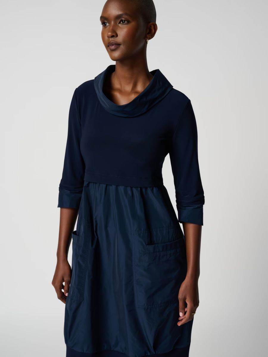 Navy blue long-sleeve dress with a cowl neckline and two front pockets on a person with dark skin tone.