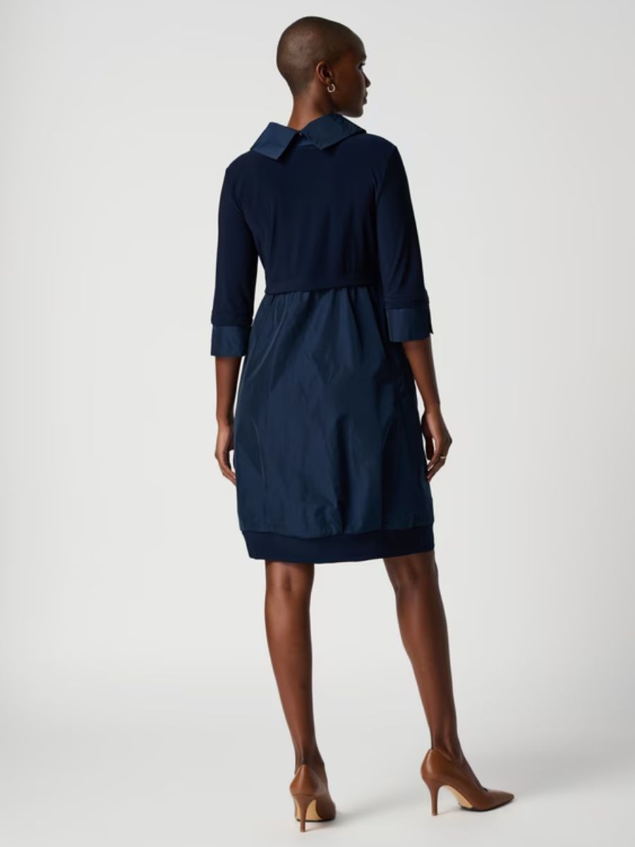 Back view of a navy blue dress with a collar and three-quarter sleeves paired with brown heels on a neutral background.
