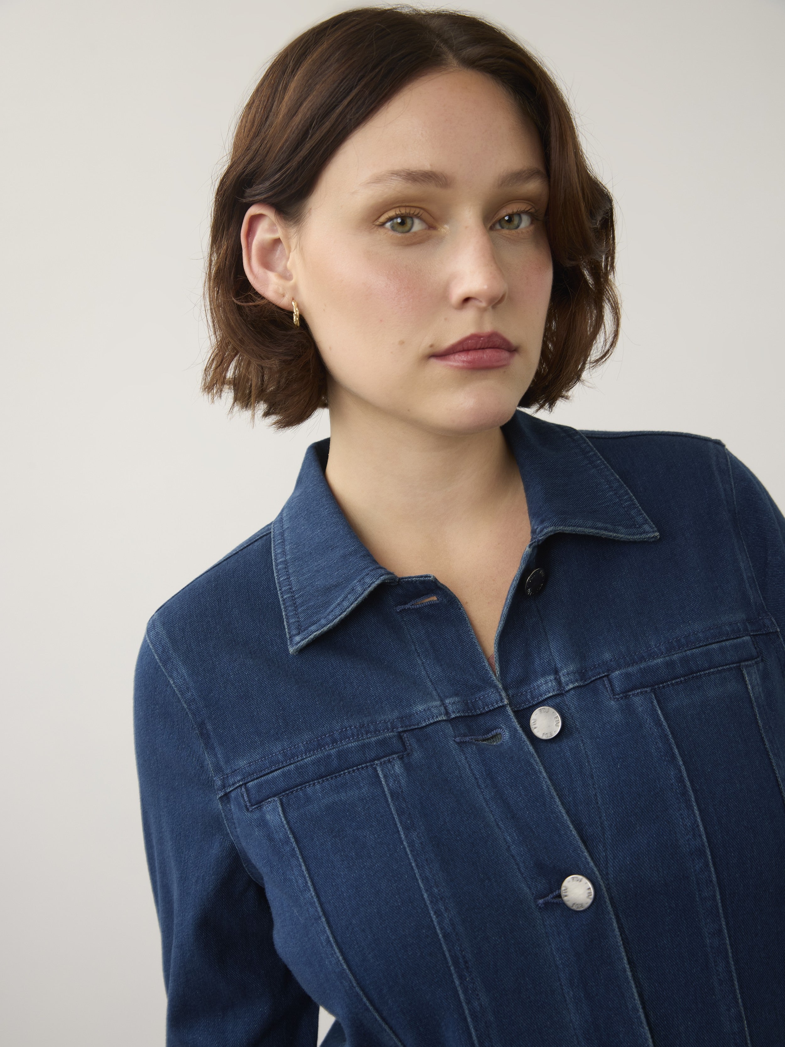 Close-up of a person wearing a dark blue denim jacket with silver buttons against a plain background.