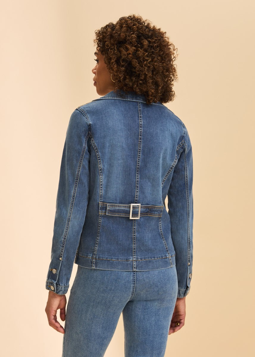 Back view of a fitted blue denim jacket with a buckle belt detail paired with blue denim jeans on a beige background.