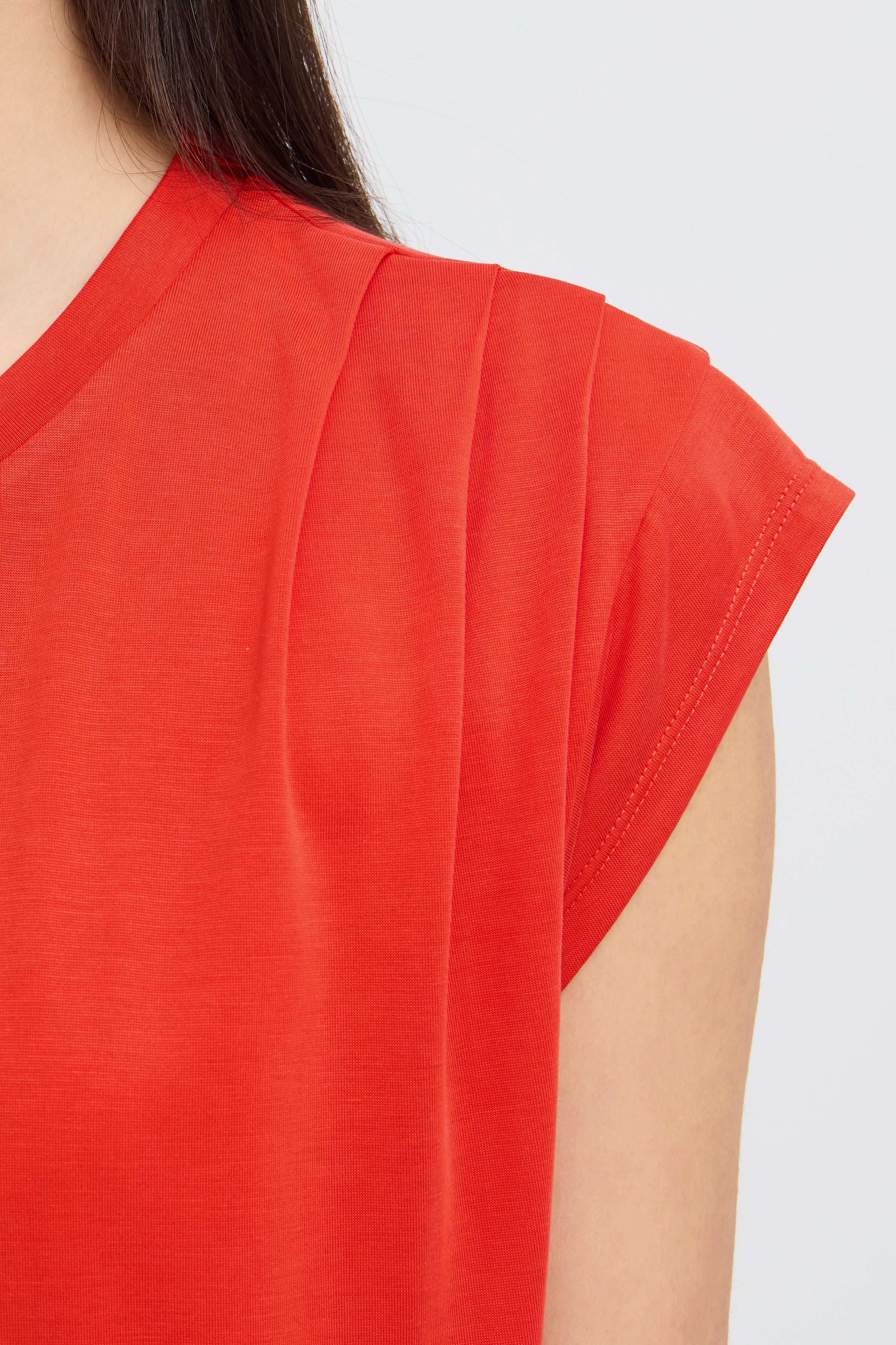Close-up of red short sleeve top with pleated shoulder detail on light background