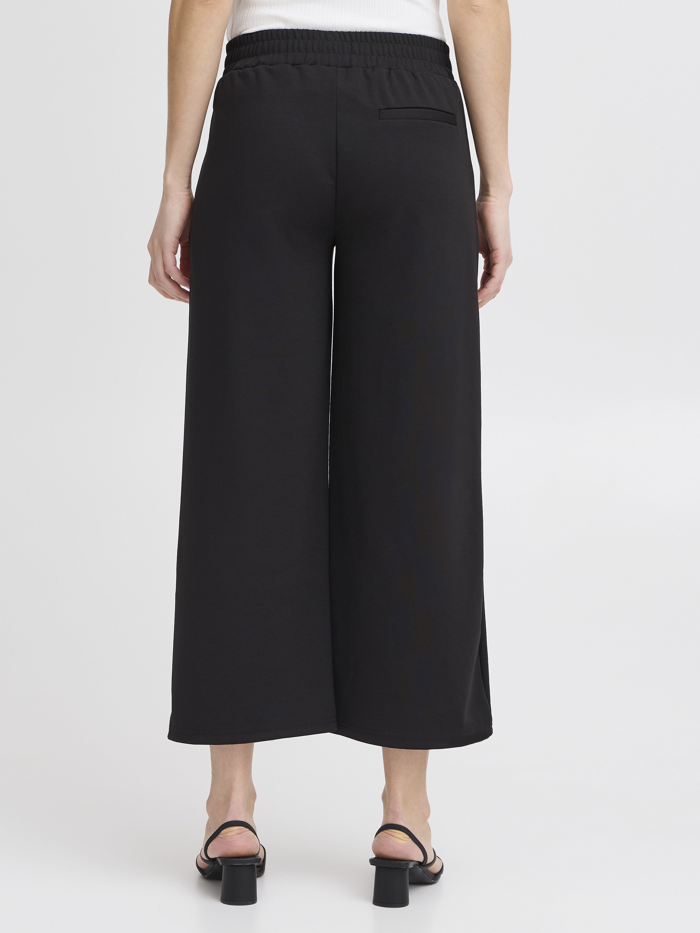 Back view of black Ichi Kate Jersey 25” Wide Pant with elastic waistband and slit hem, paired with black heeled sandals.