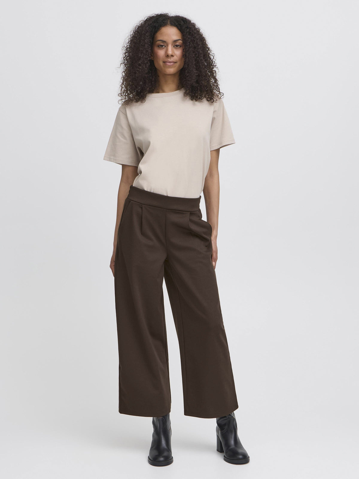 Beige short-sleeve top with brown wide-leg trousers and black ankle boots against a light gray background