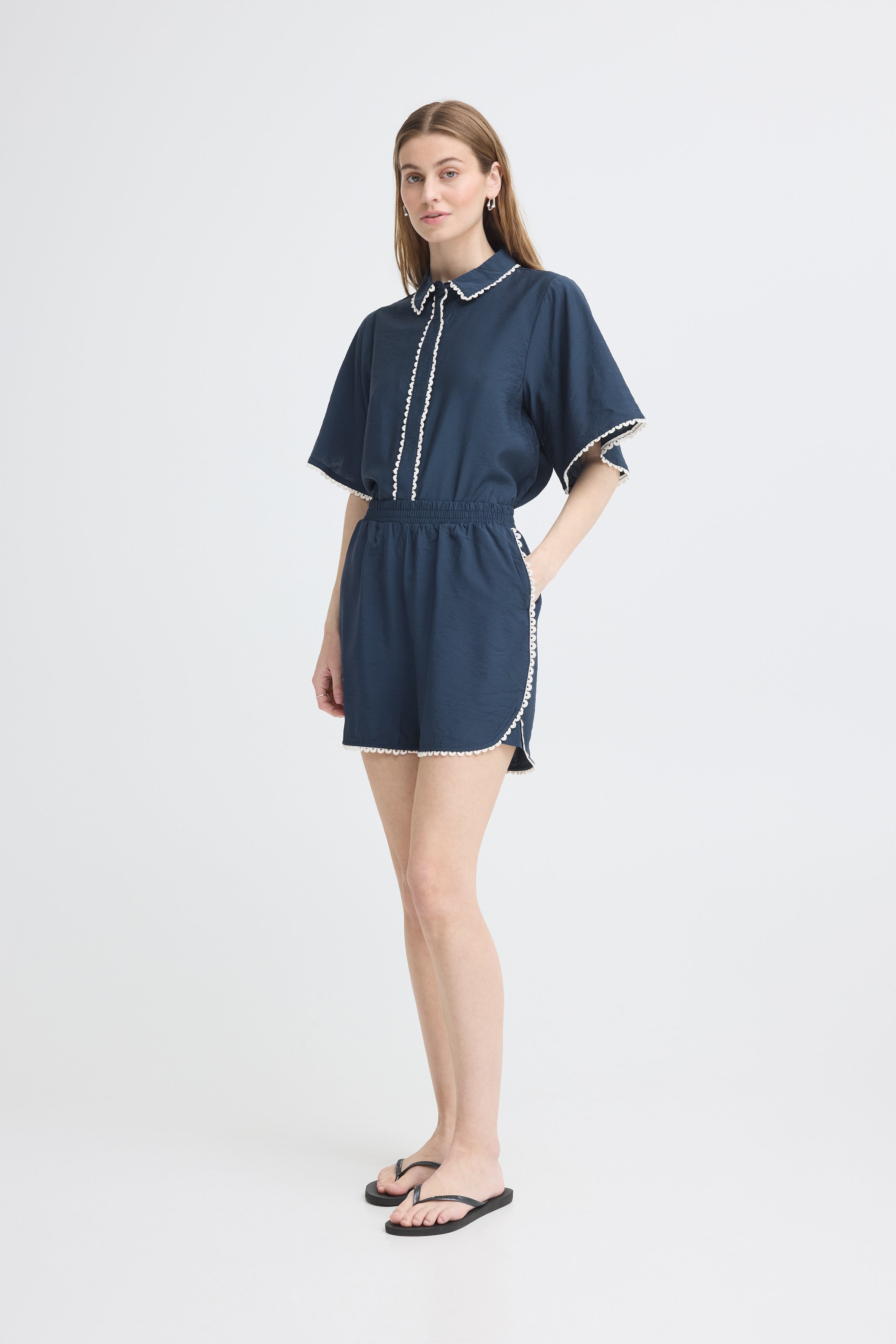 Navy short-sleeve romper with white trim detailing paired with black flip-flops on light background.