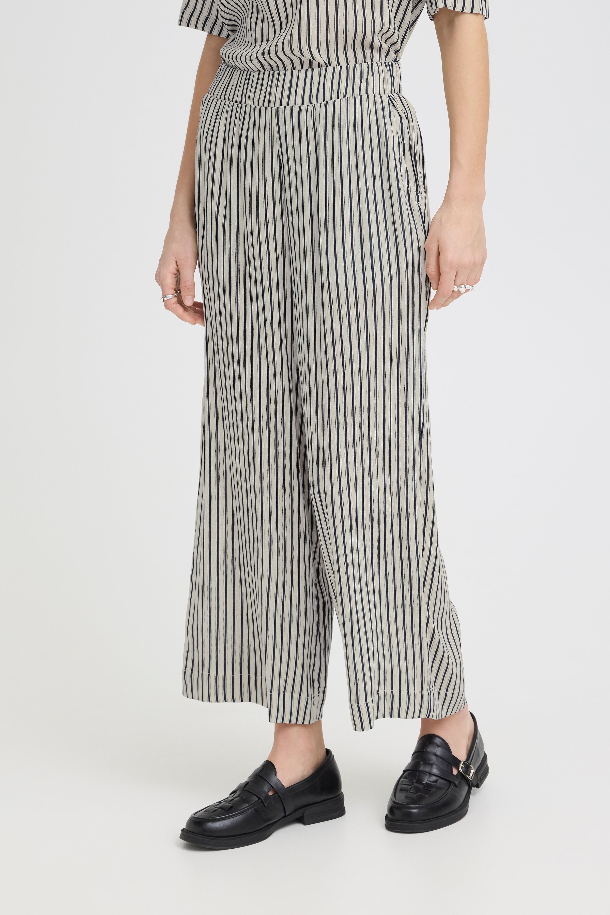 Ichi Marrakech Cropped Trousers in beige with black vertical stripes, styled with black leather loafers.