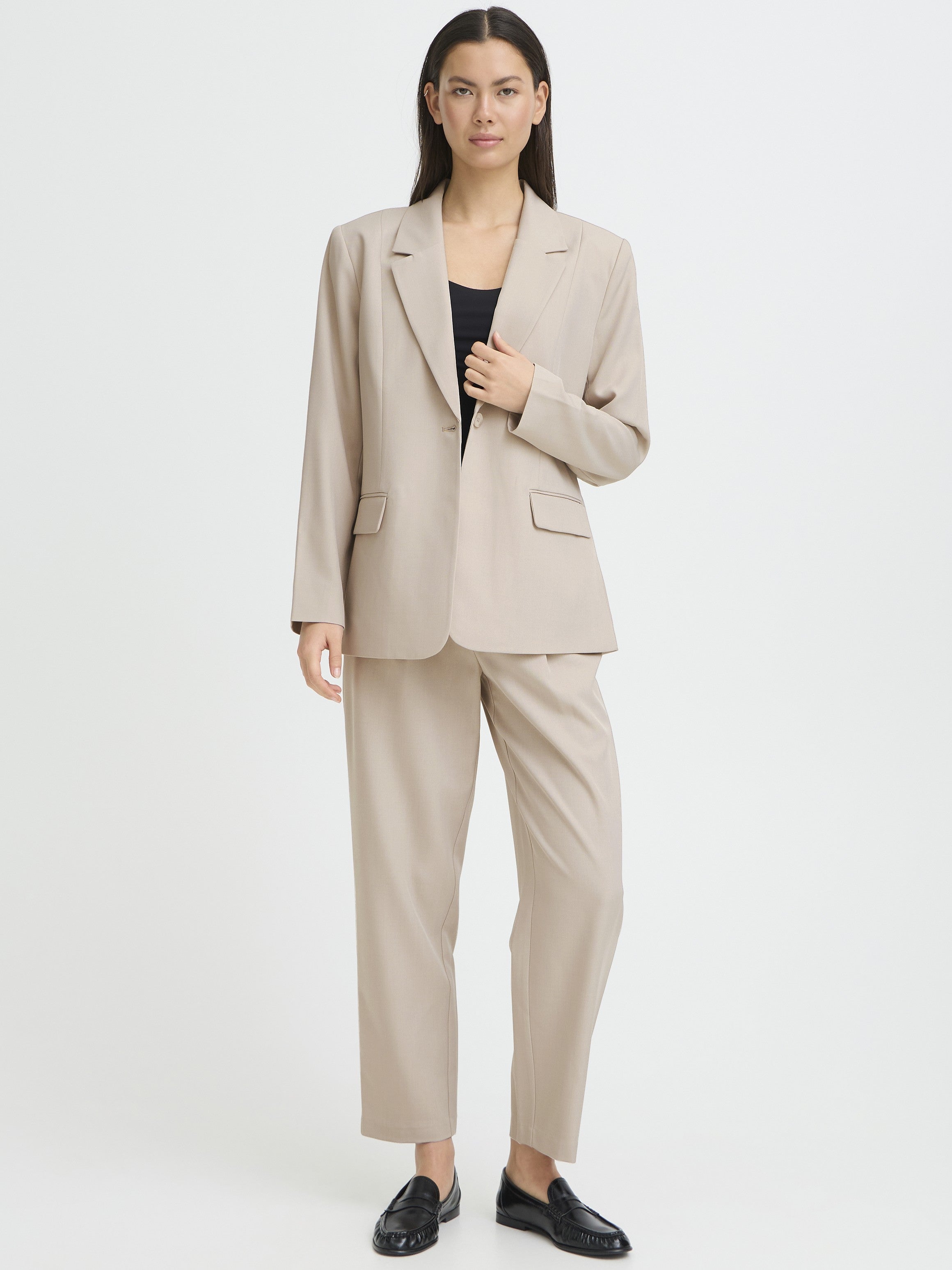 Beige tailored suit jacket and matching trousers paired with a black top and black loafers on a neutral background.