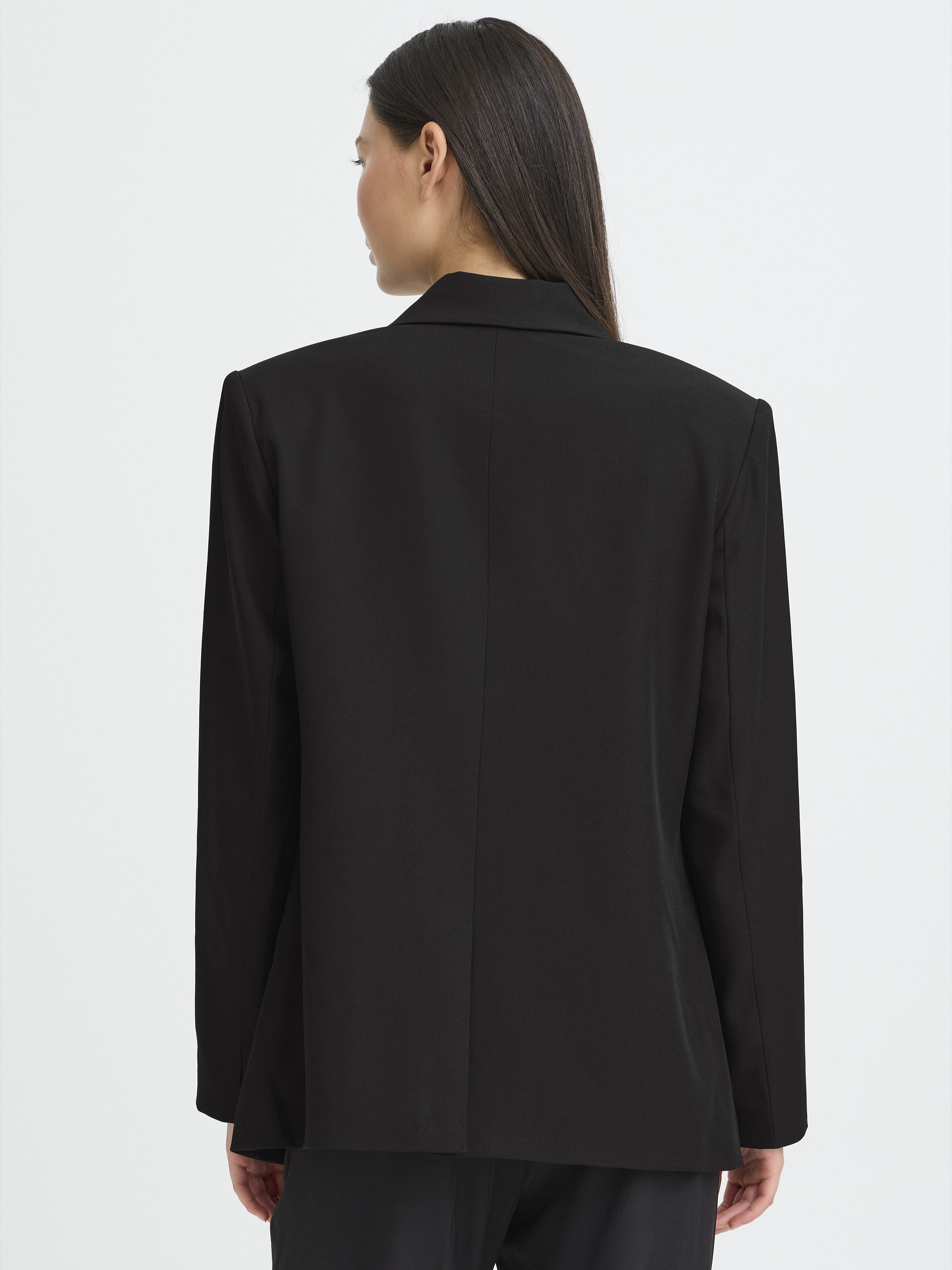 Back view of a black tailored jacket with long sleeves and a center back seam on a light background.