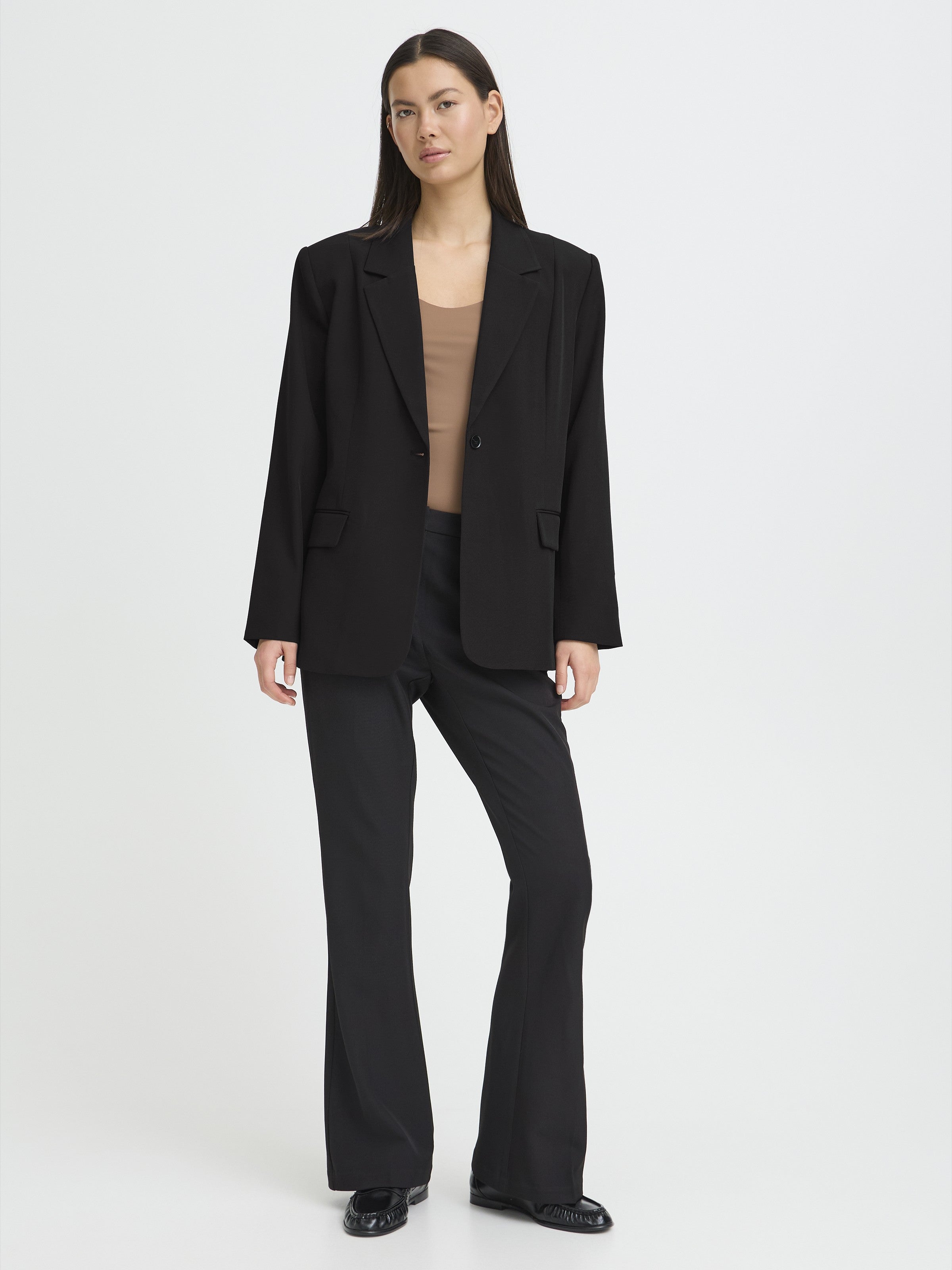 Black oversized blazer paired with black flared pants and a beige fitted top on a neutral background