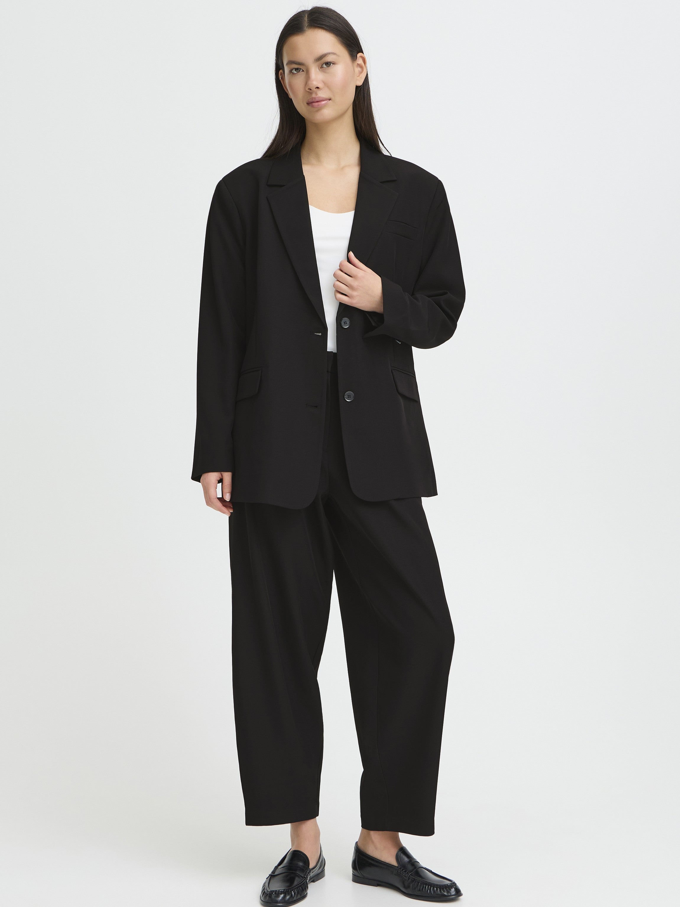 Black oversized blazer and matching wide-leg trousers paired with a white top and black loafers on a plain background