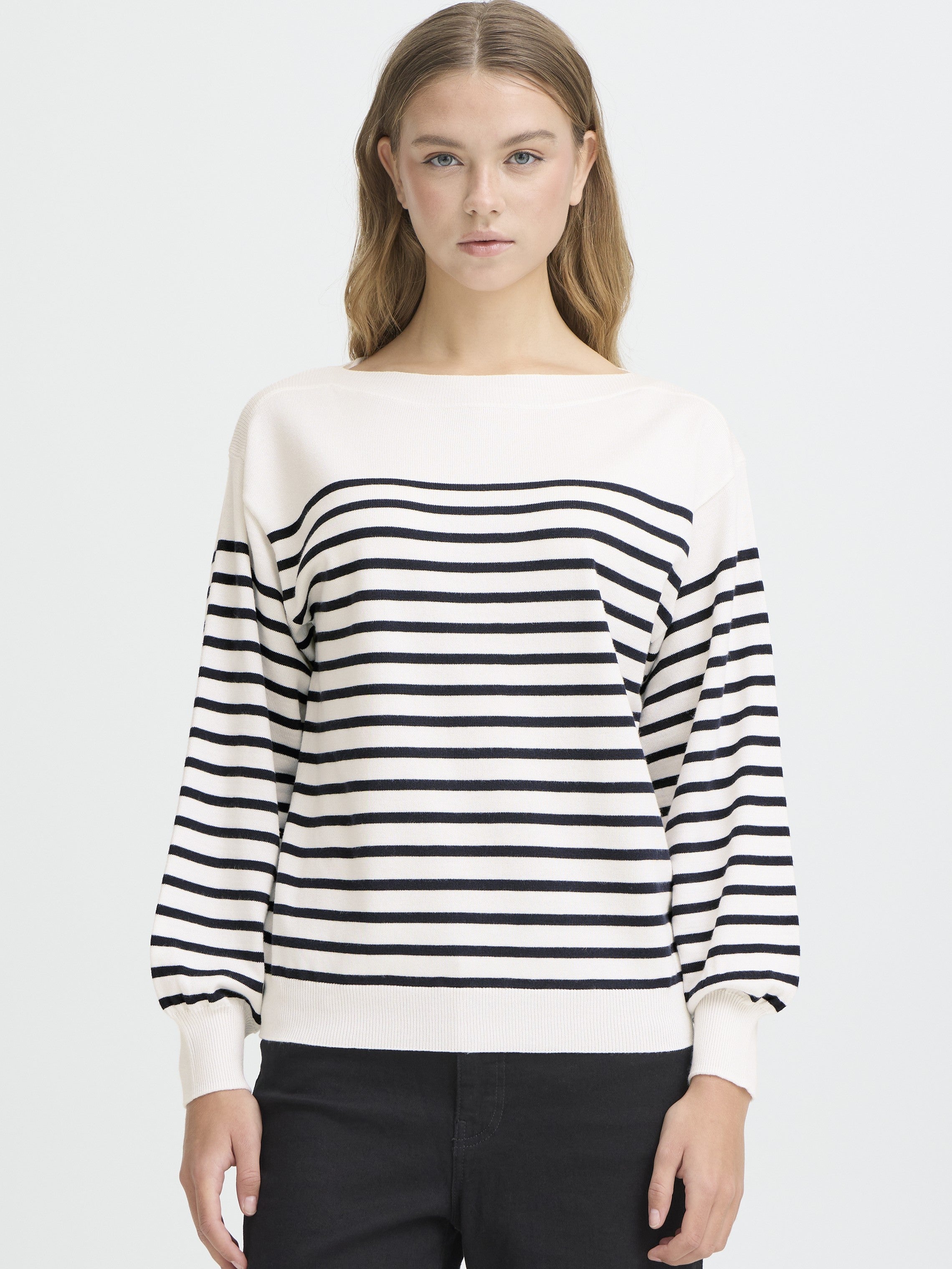 Model in white and black striped Ichi Boat Neck Sweater paired with black pants in a minimalist studio setting