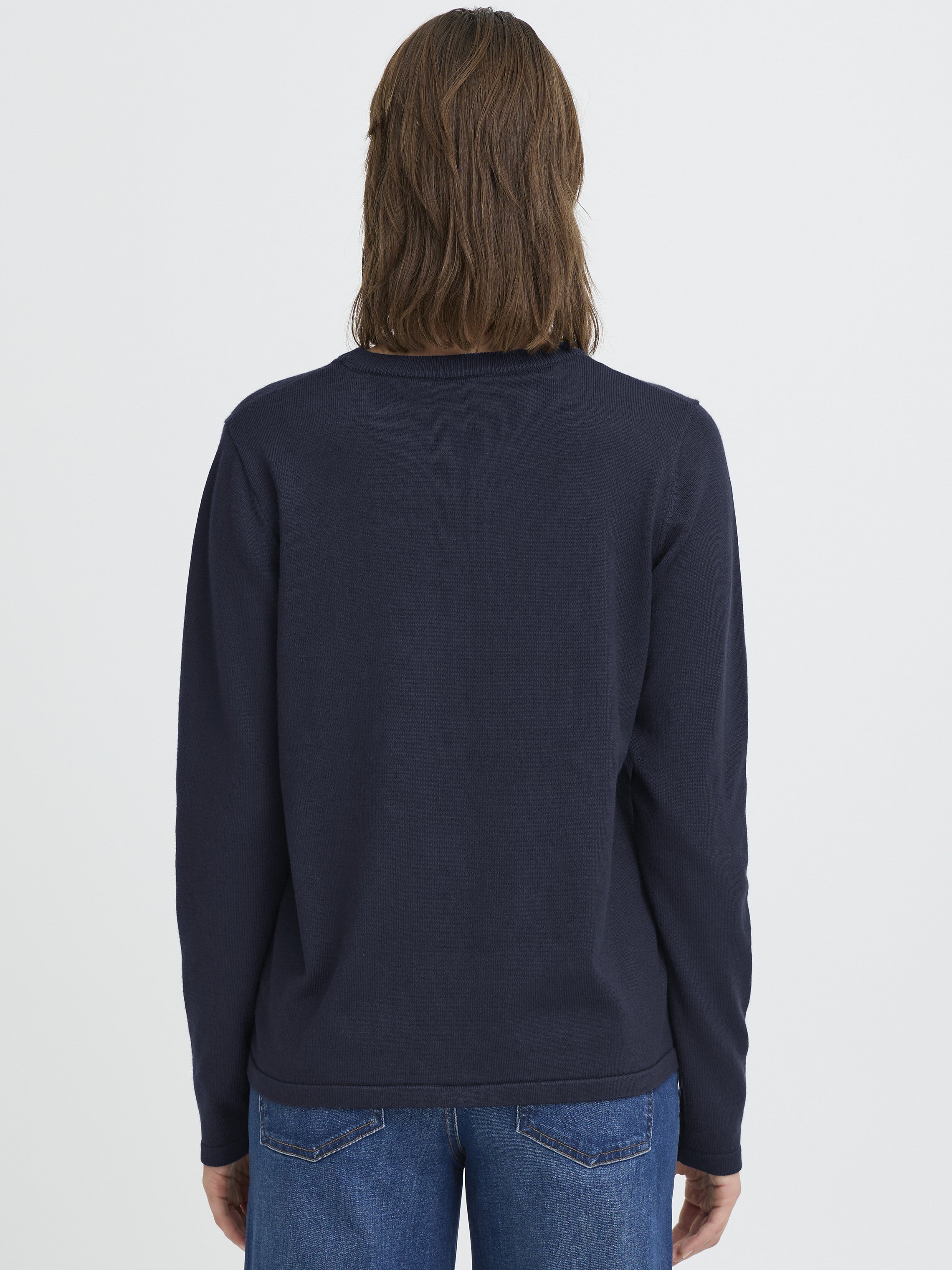 Back view of a navy blue long-sleeve sweater paired with medium blue denim jeans on a neutral background.