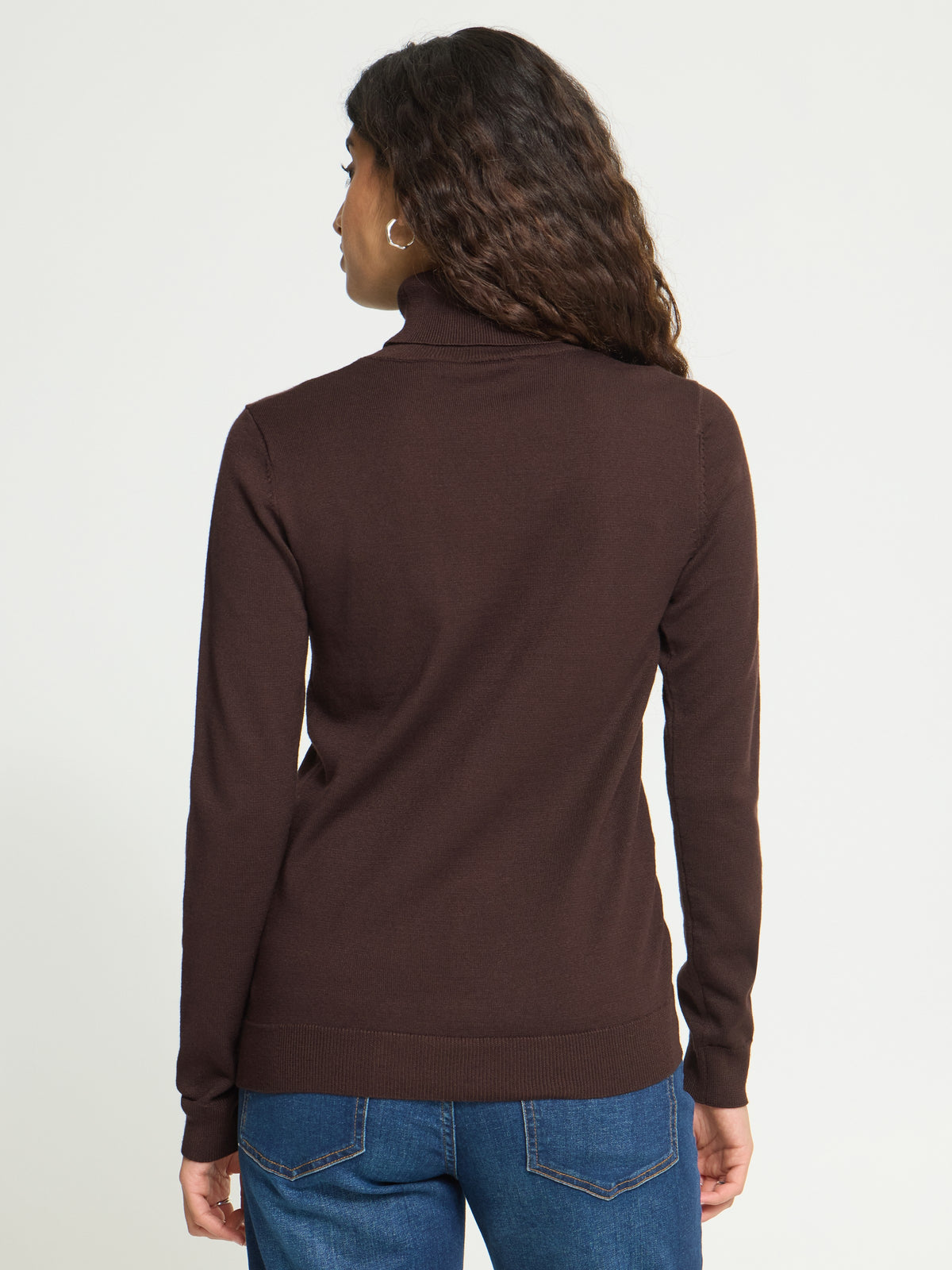 Back view of a long-sleeve, dark brown turtleneck sweater paired with blue denim jeans.