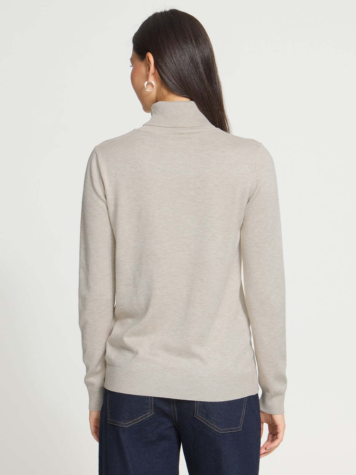 Back view of a light beige turtleneck sweater paired with dark blue denim jeans against a plain background.