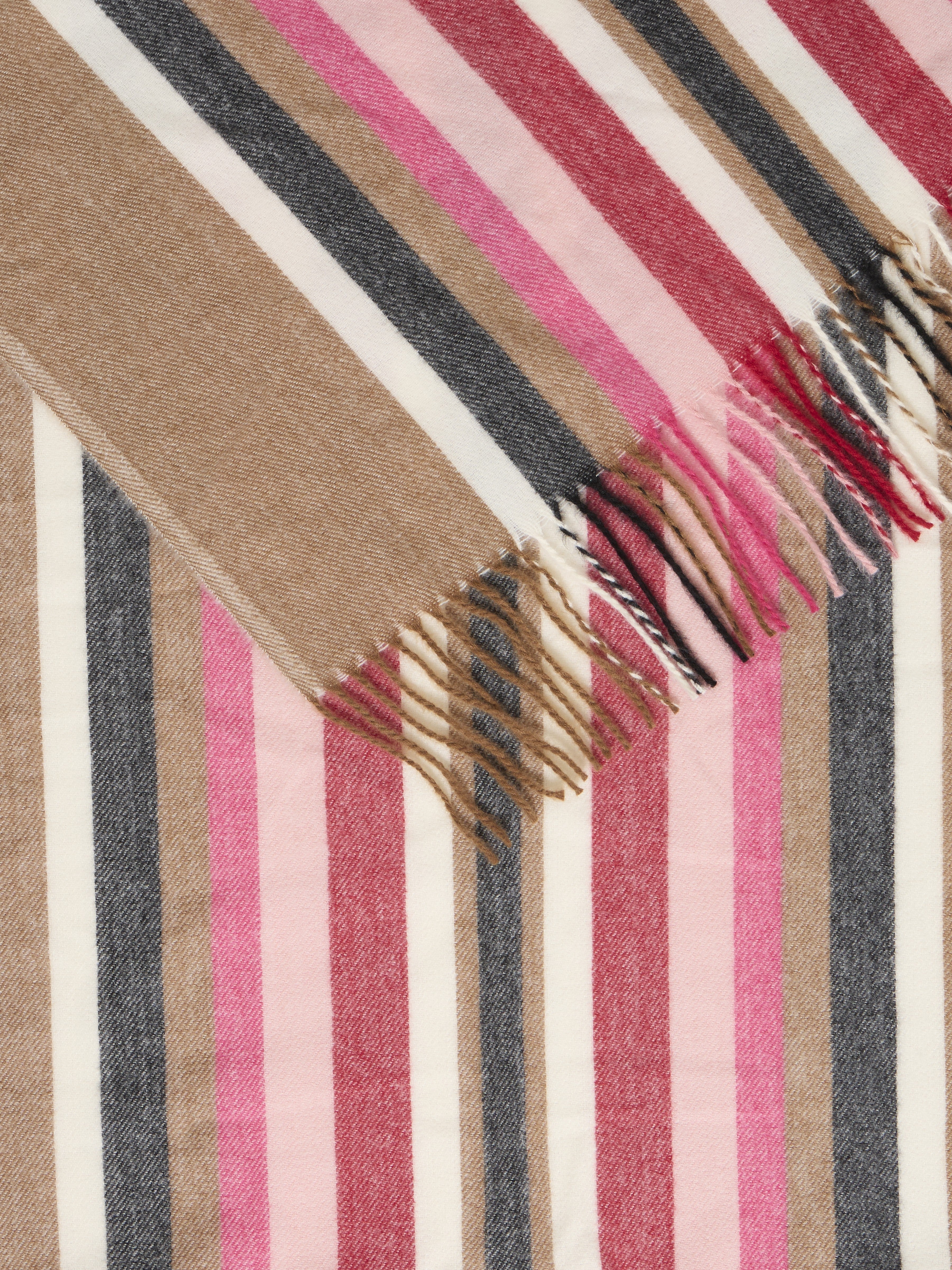 Close-up of a woven fabric with vertical stripes in beige, pink, red, black, and white, featuring fringed edges.