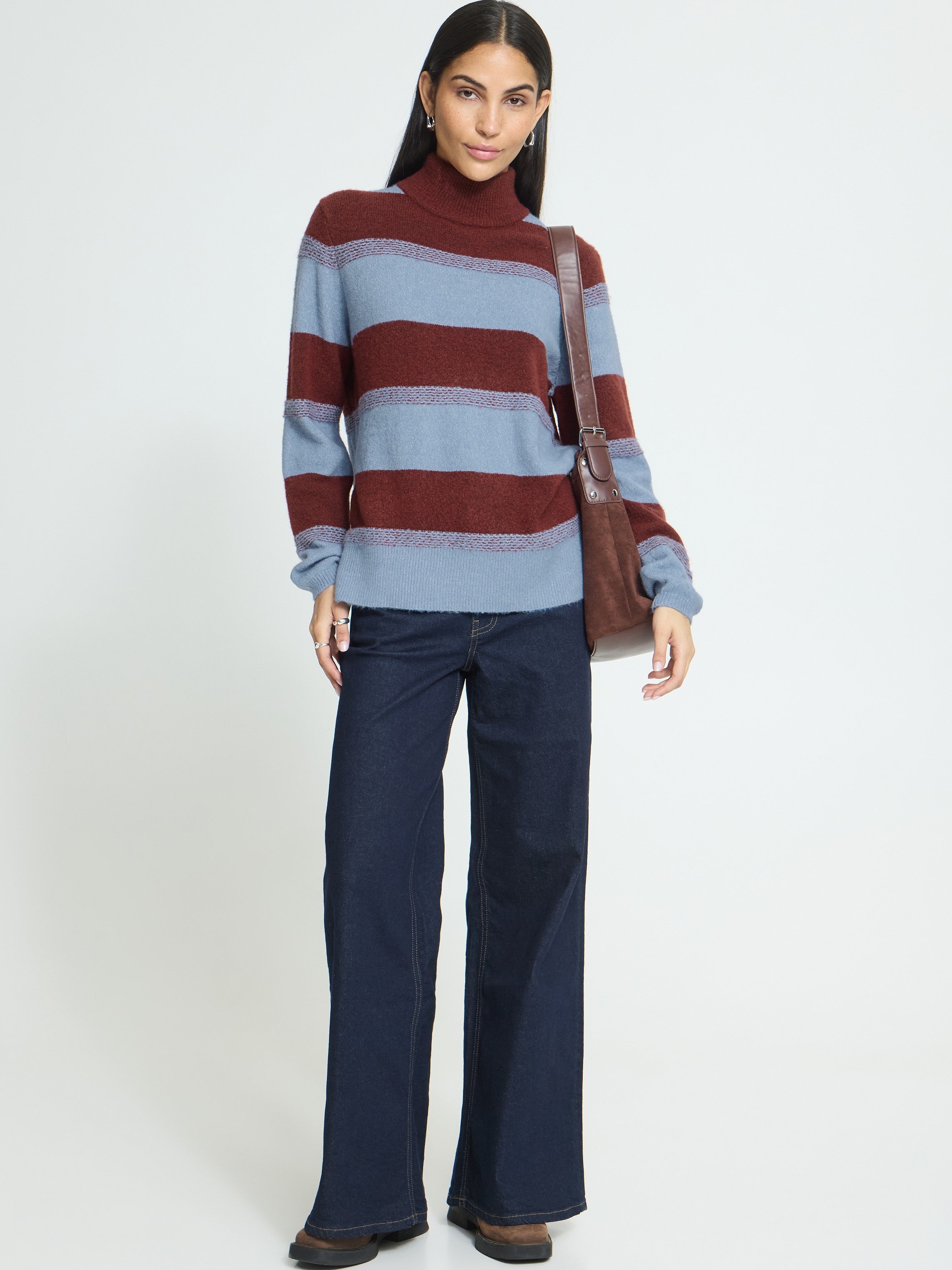 Striped high-neck sweater paired with dark wide-leg denim jeans and a brown shoulder bag against a plain background.