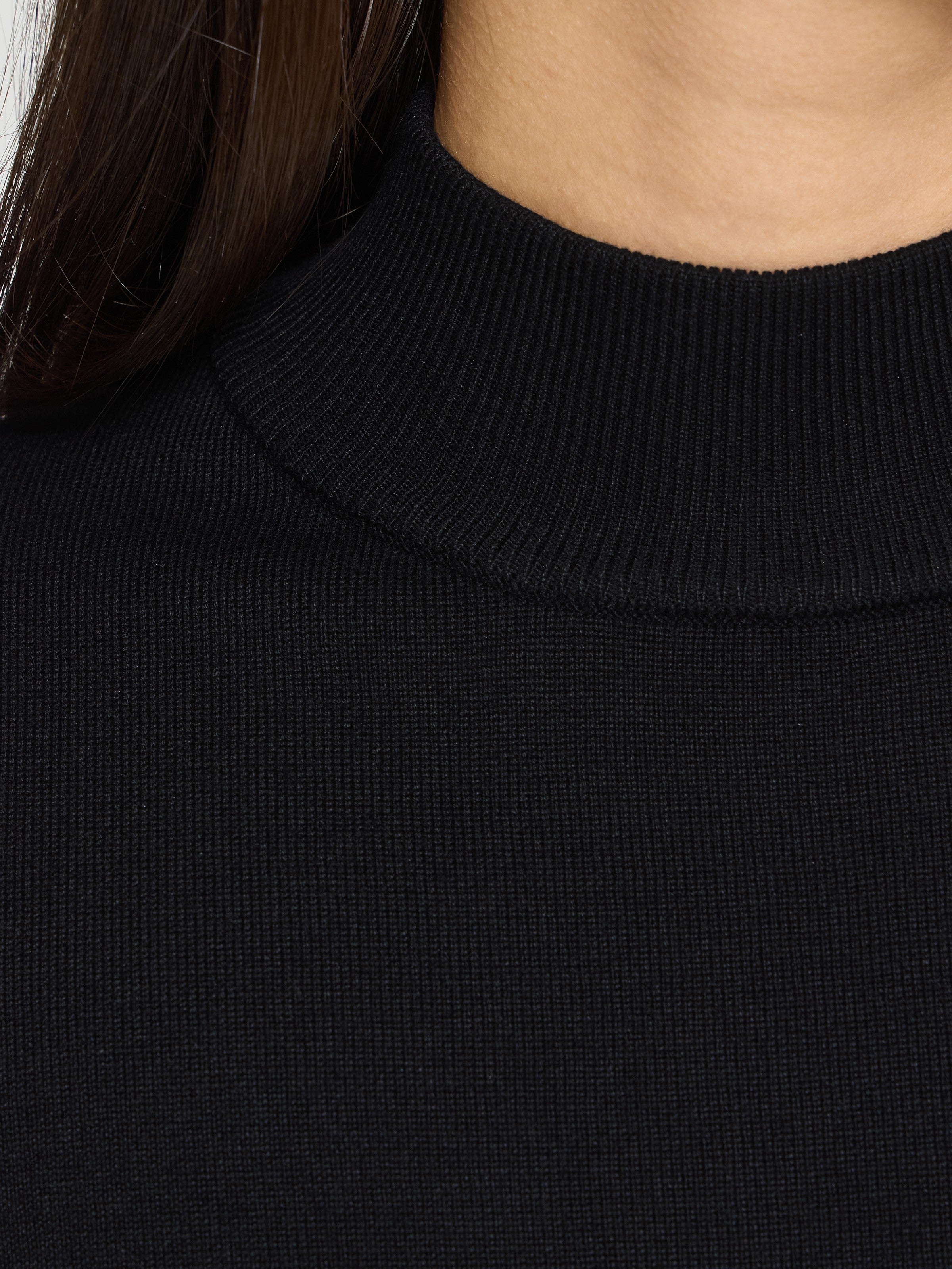 Close-up of a black ribbed knit sweater neckline and upper chest area against a neutral background.