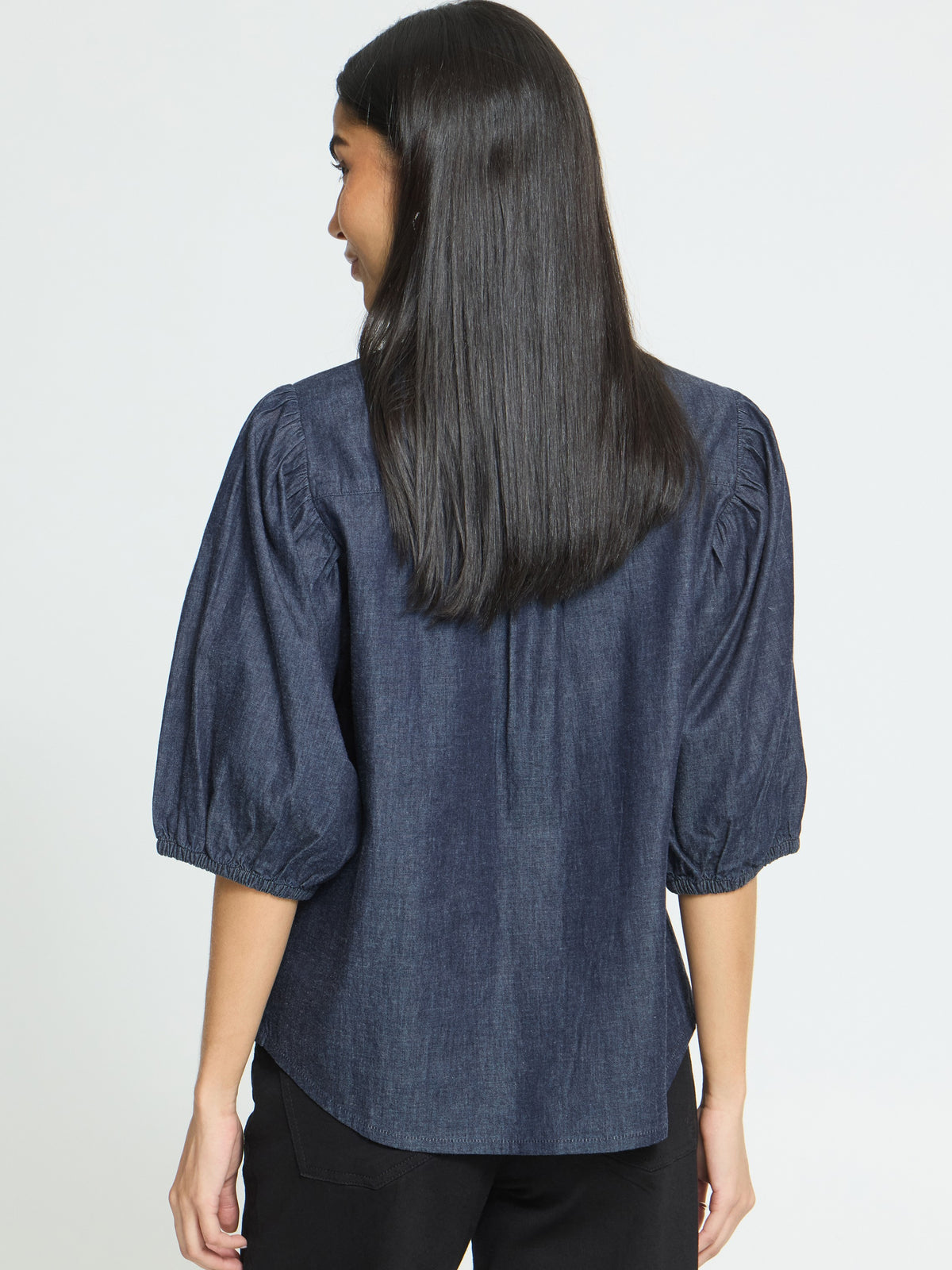 Back view of a denim top with three-quarter puff sleeves and gathered shoulder details