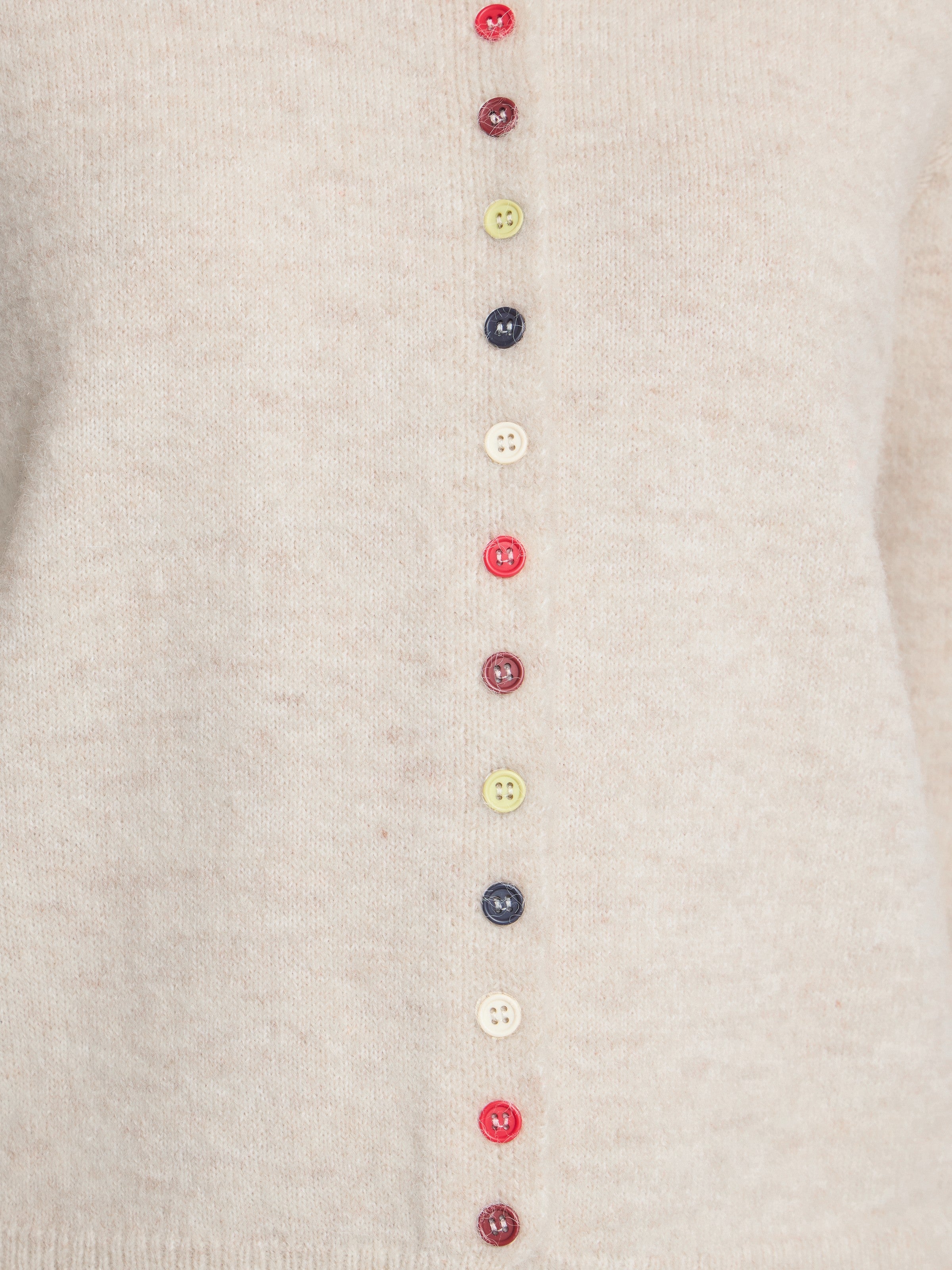 Close-up of a beige knitted sweater with a vertical row of colorful buttons in red, yellow, navy, and white.