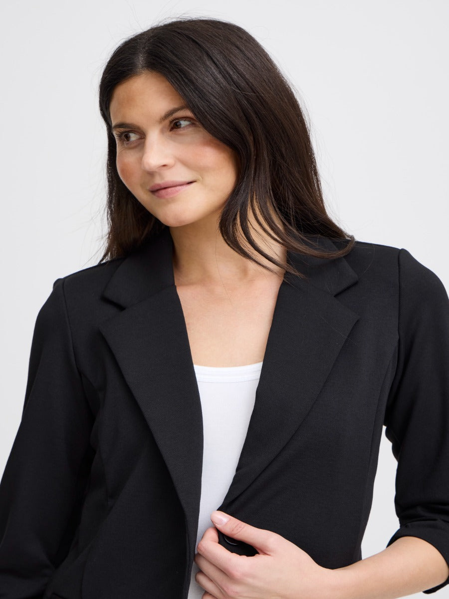Close-up of a black tailored jacket over a white top with a notched lapel collar and three-quarter sleeves