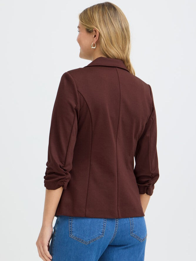 Back view of a person in a fitted brown blazer with ruched sleeves and blue denim jeans