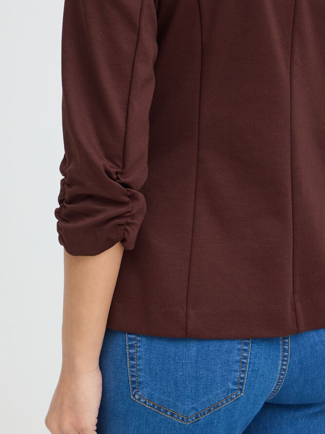 Close-up of a brown ruched sleeve top paired with blue denim jeans from the back view.