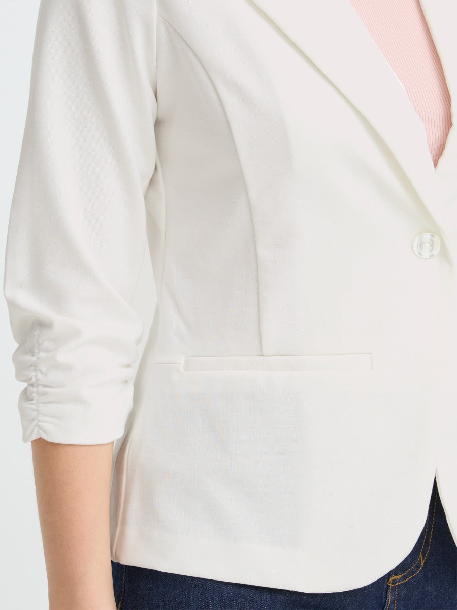 Close-up of an off-white jacket sleeve and side pocket with a single button and ruched detailing on the arm