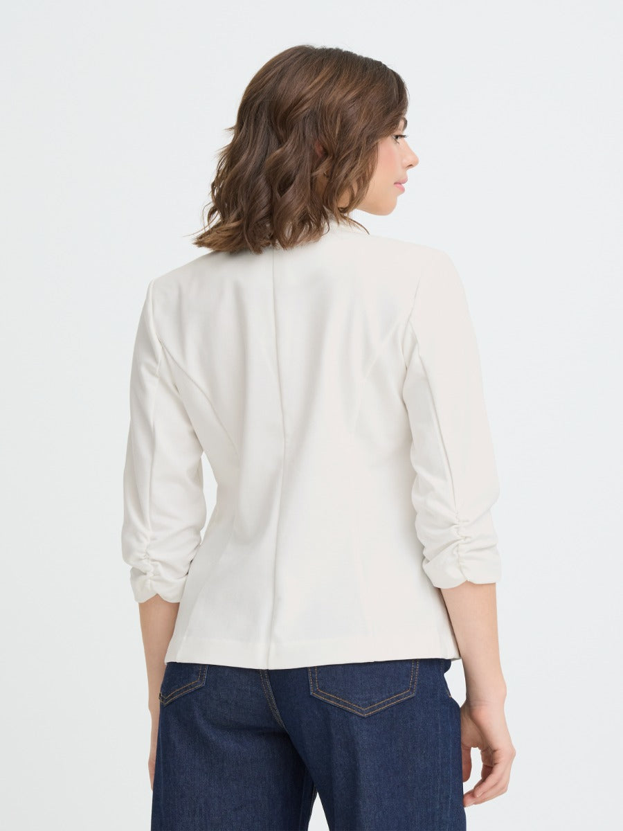 Back view of a cream-colored fitted blazer with ruched sleeves paired with dark blue denim jeans.