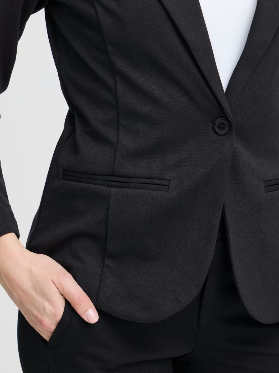 Close-up of a black tailored jacket with side pockets and a single-button closure over black pants.