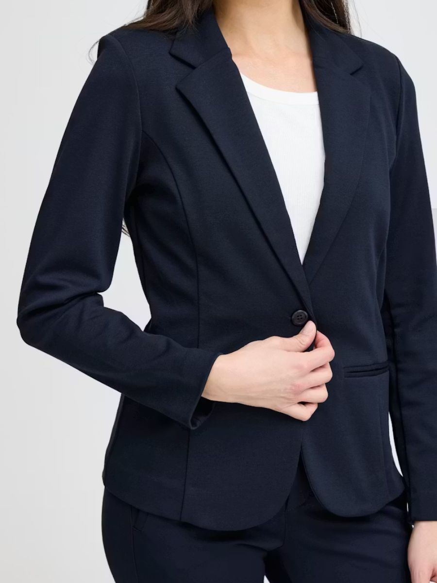 Close-up of a navy tailored blazer with a single button over a white top, styled with matching navy pants.