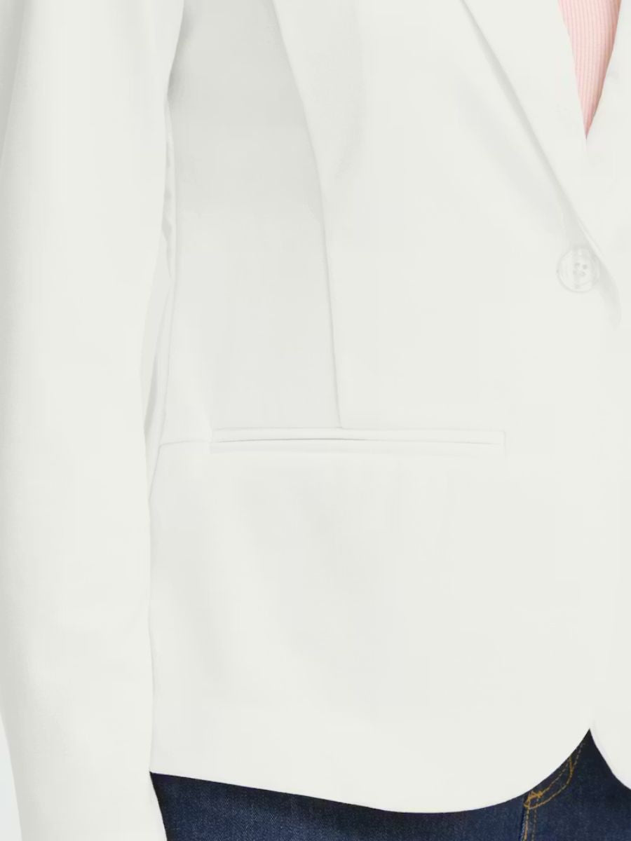 Close-up of an off-white tailored blazer with a single button and welt pocket over dark denim jeans.