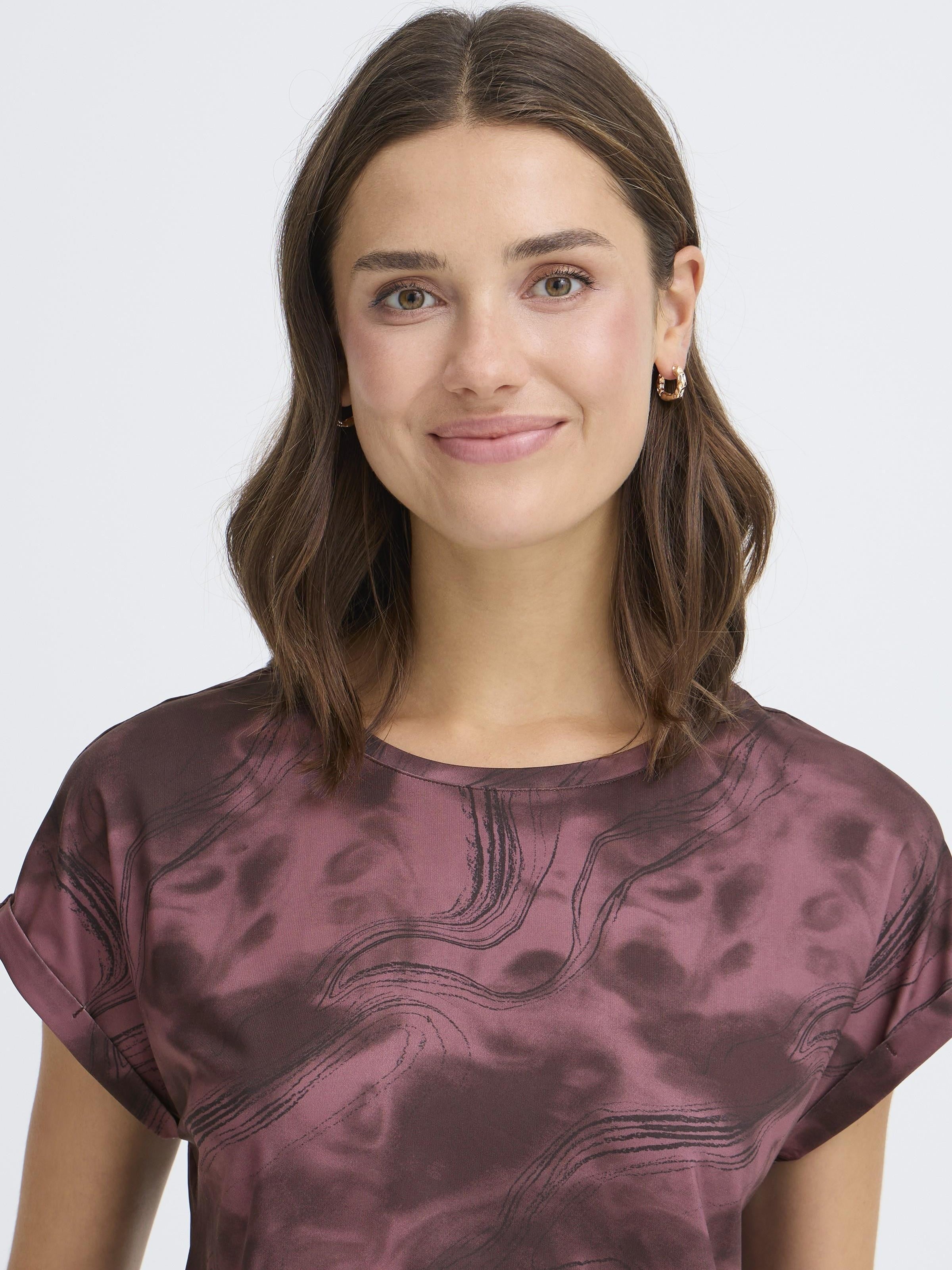 Smiling model wearing a burgundy Fransa Seen Short Sleeve Crew Neck Top with subtle abstract pattern and gold hoop earrings