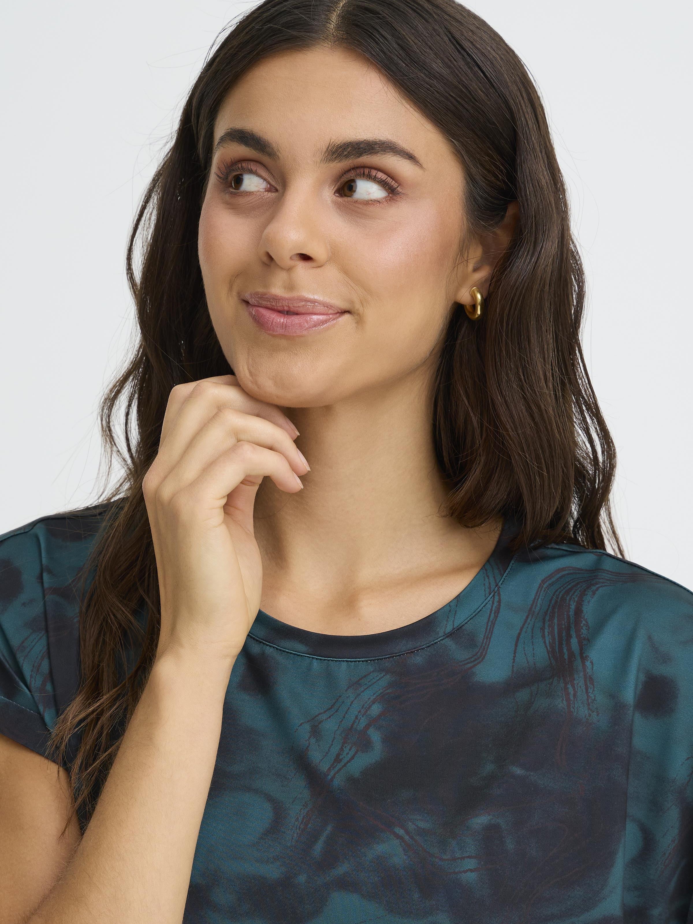 Close-up of a dark green patterned Fransa Seen Short Sleeve Crew Neck Top on a model with hoop earrings