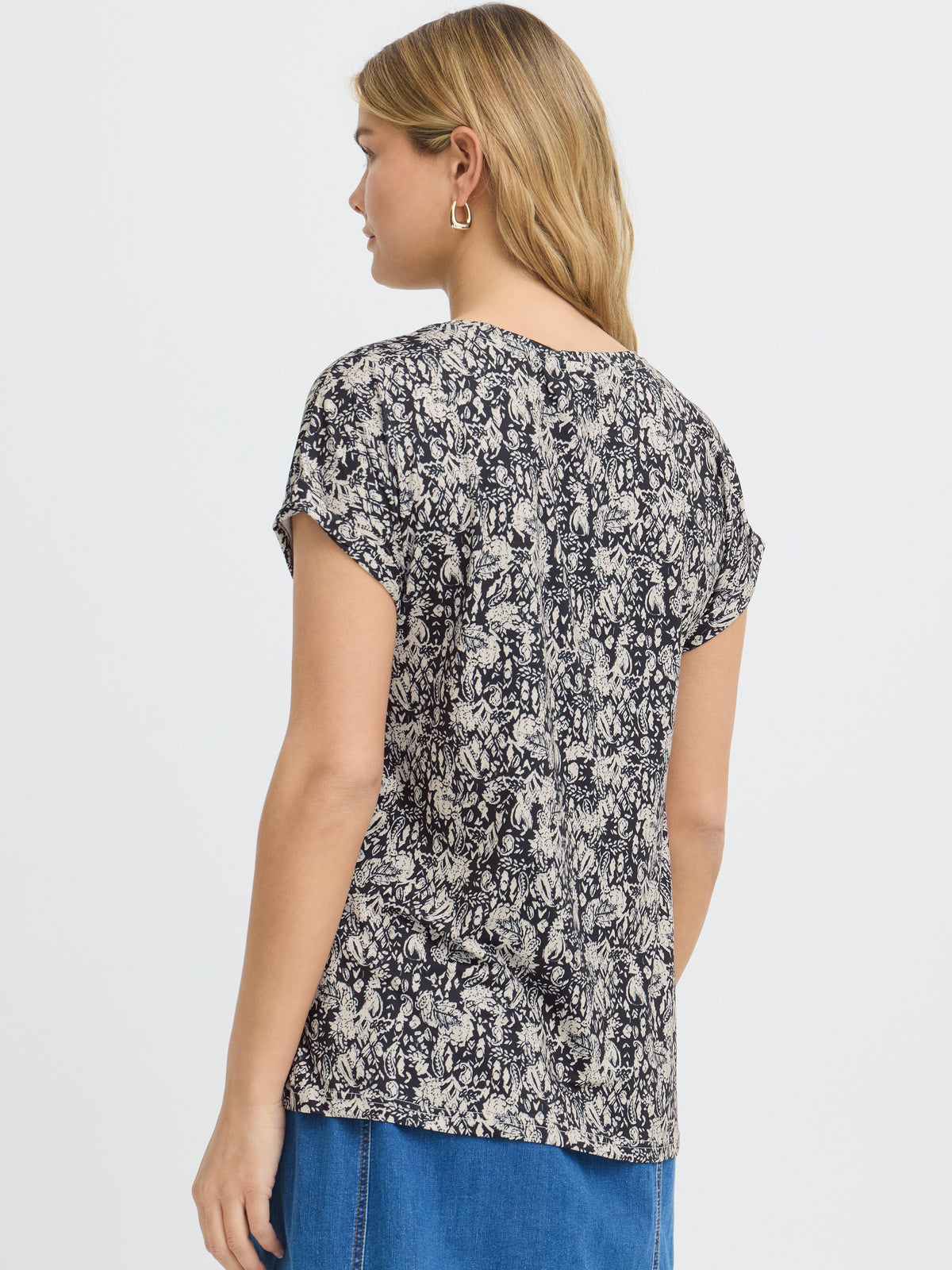 Back view of a short-sleeve black and white floral print top with blue denim bottoms