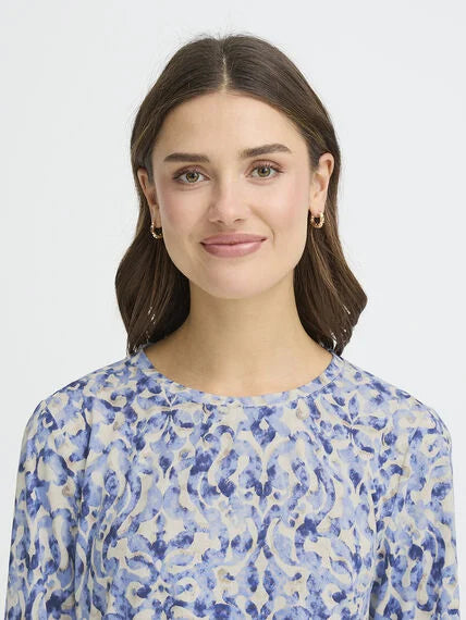 Close-up of a model wearing a blue patterned Fransa Seen Three-Quarter Sleeve Cuff Top with gold hoop earrings