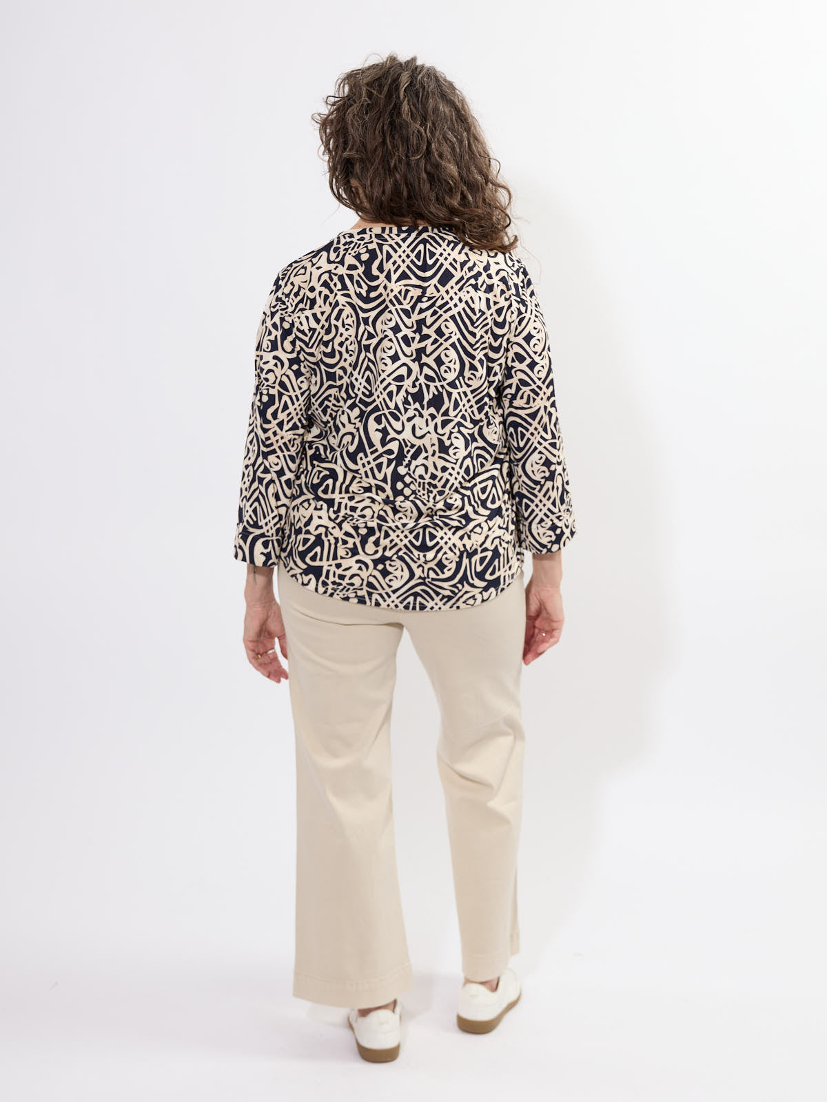 Fransa Seen Three-Quarter Sleeve Cuff Top with abstract navy and beige pattern, styled with beige pants and white shoes.