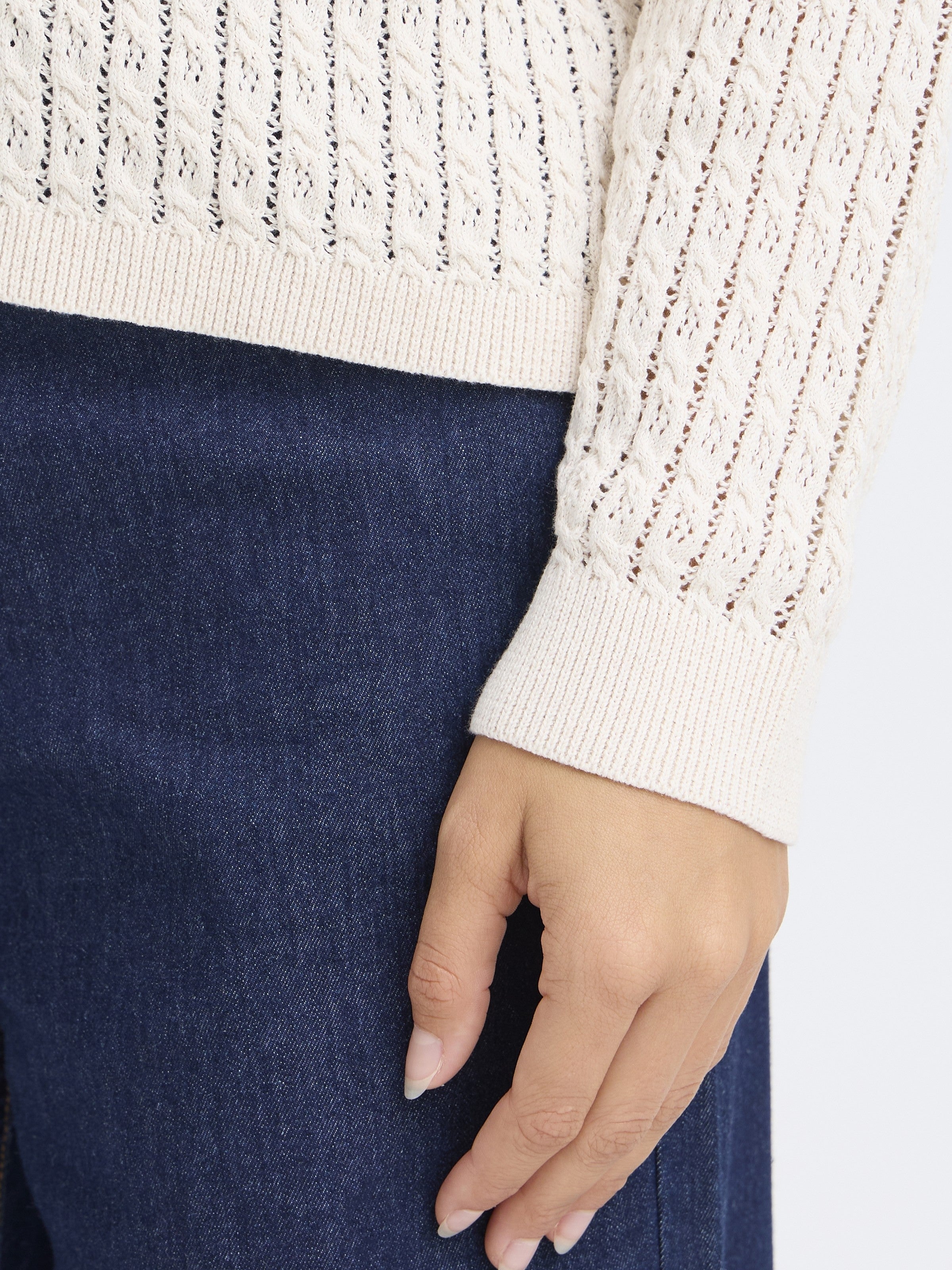 Close-up of a hand next to a white Fransa Sammy Mini Cable Knit Crew Neck Sweater sleeve and dark denim pants