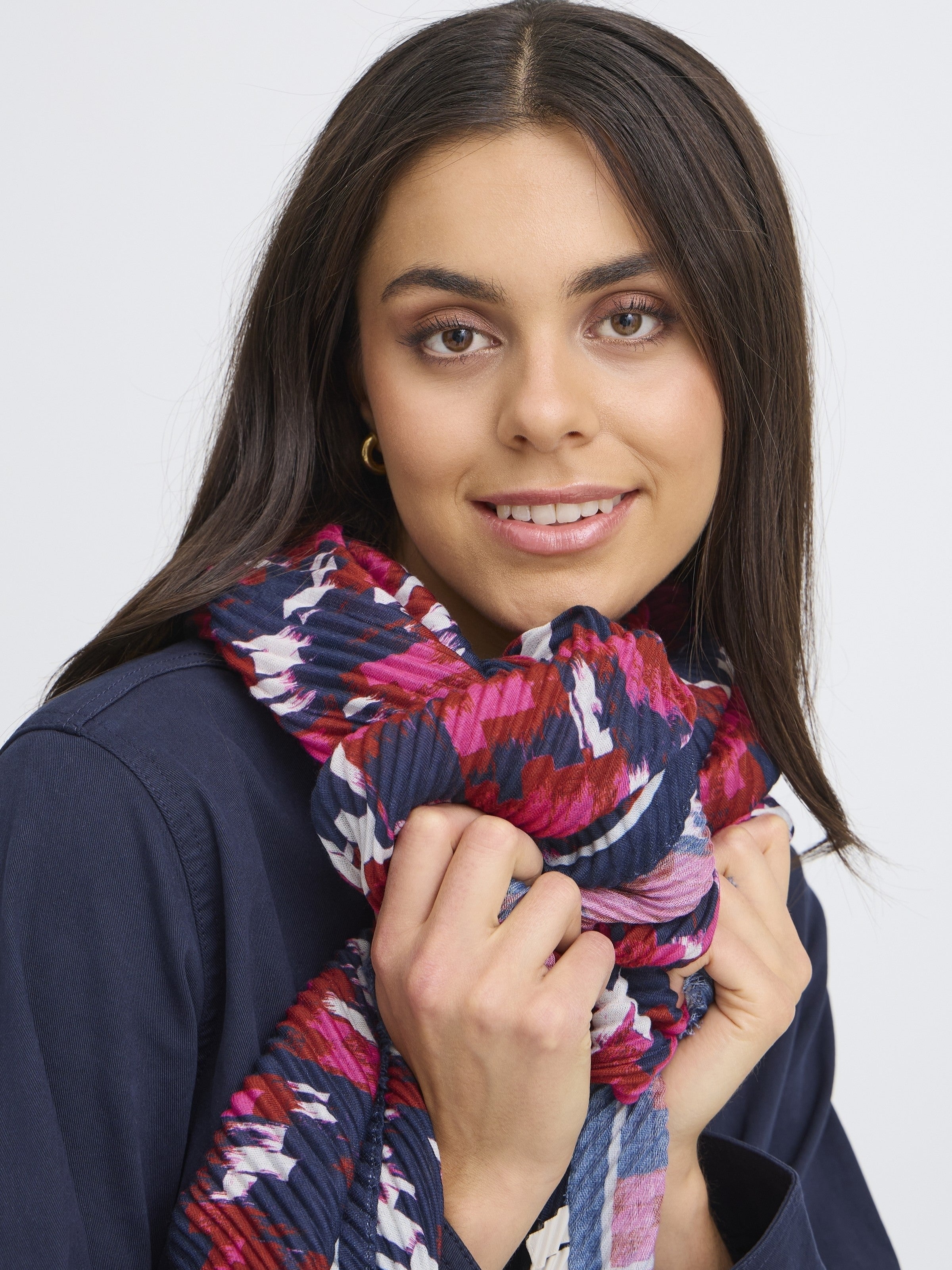 Close-up of a smiling person holding a Fransa Plisea Printed Lightweight Scarf with berry and navy print accessory