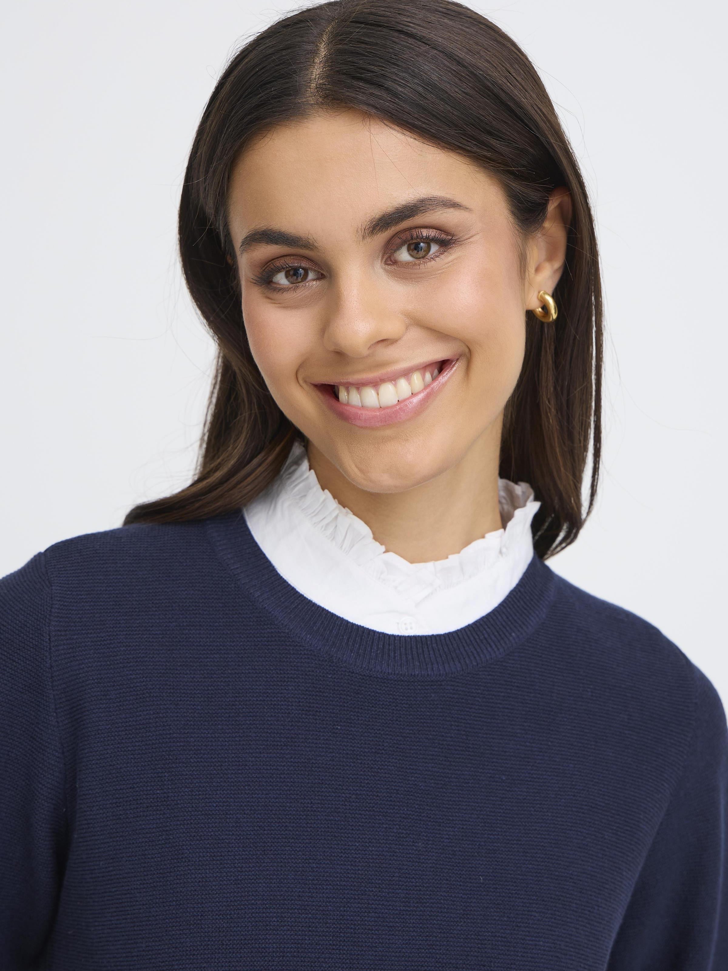 Close-up of a smiling person wearing a white Fransa Somia Ruffle Dickie Collar under a navy sweater by Fransa.