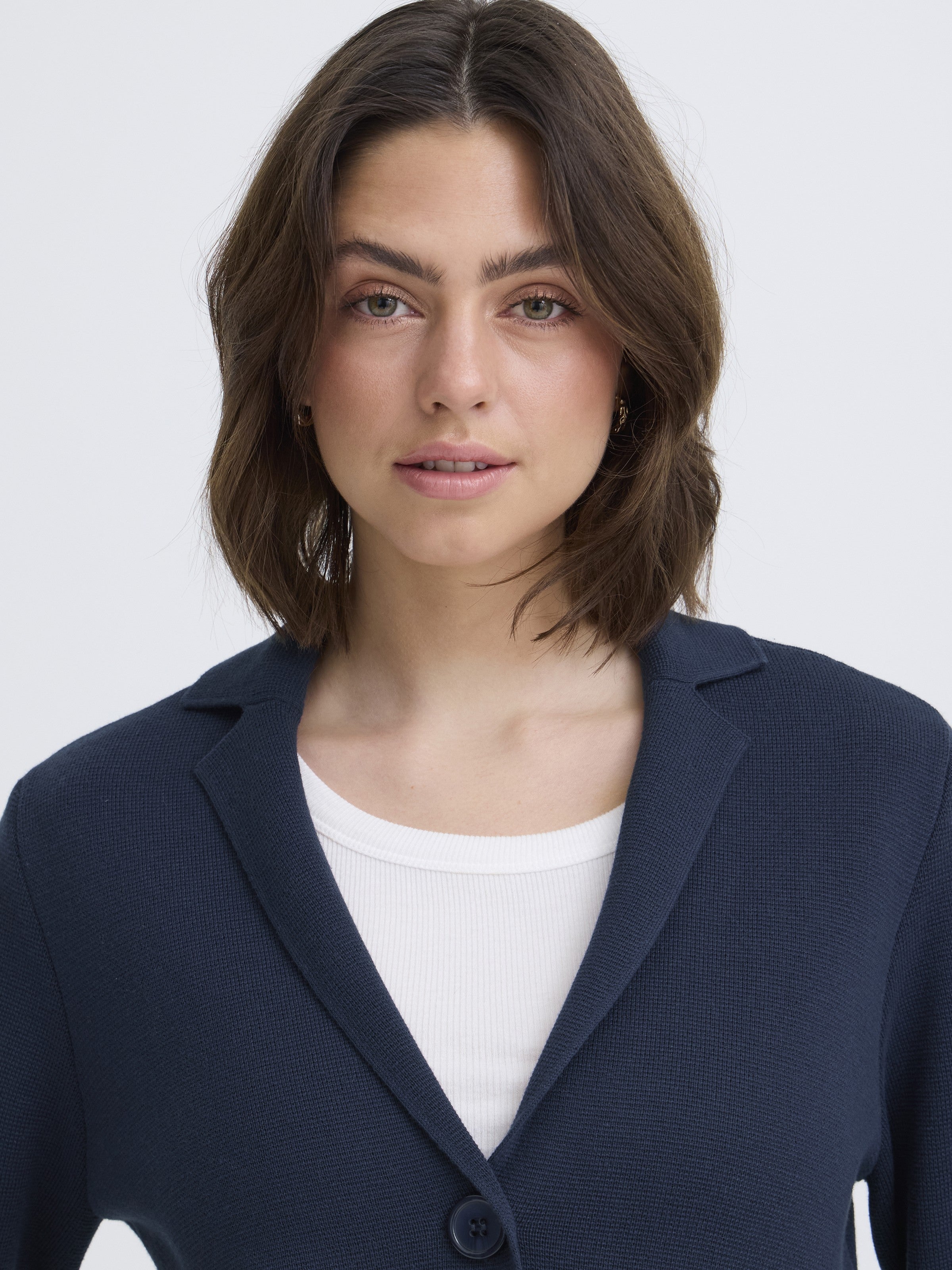 Close-up of a model wearing a navy Fransa Frita Three-Button Pocket Cardigan over a white top from Fransa Sweaters.