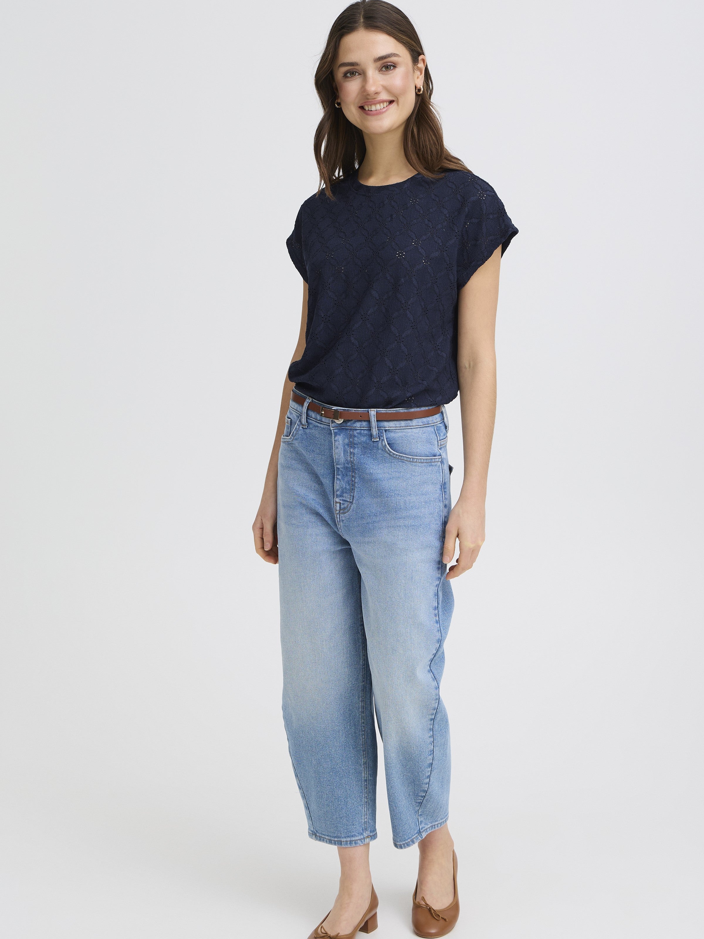Model wearing Fransa Mira Eyelet Stretch Short Sleeve Top in navy paired with light blue jeans and brown shoes.