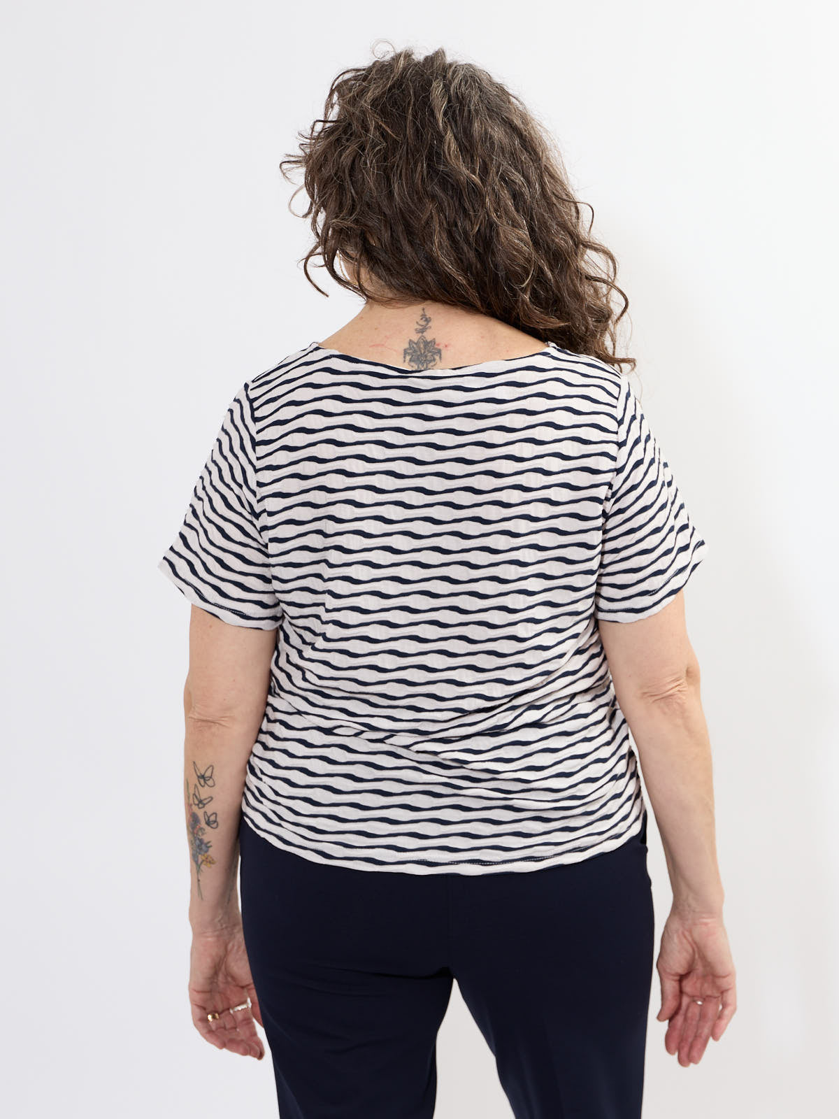 Back view of Fransa Niamy Textured Wave Short Sleeve Top in white with navy wave pattern, styled with dark pants.
