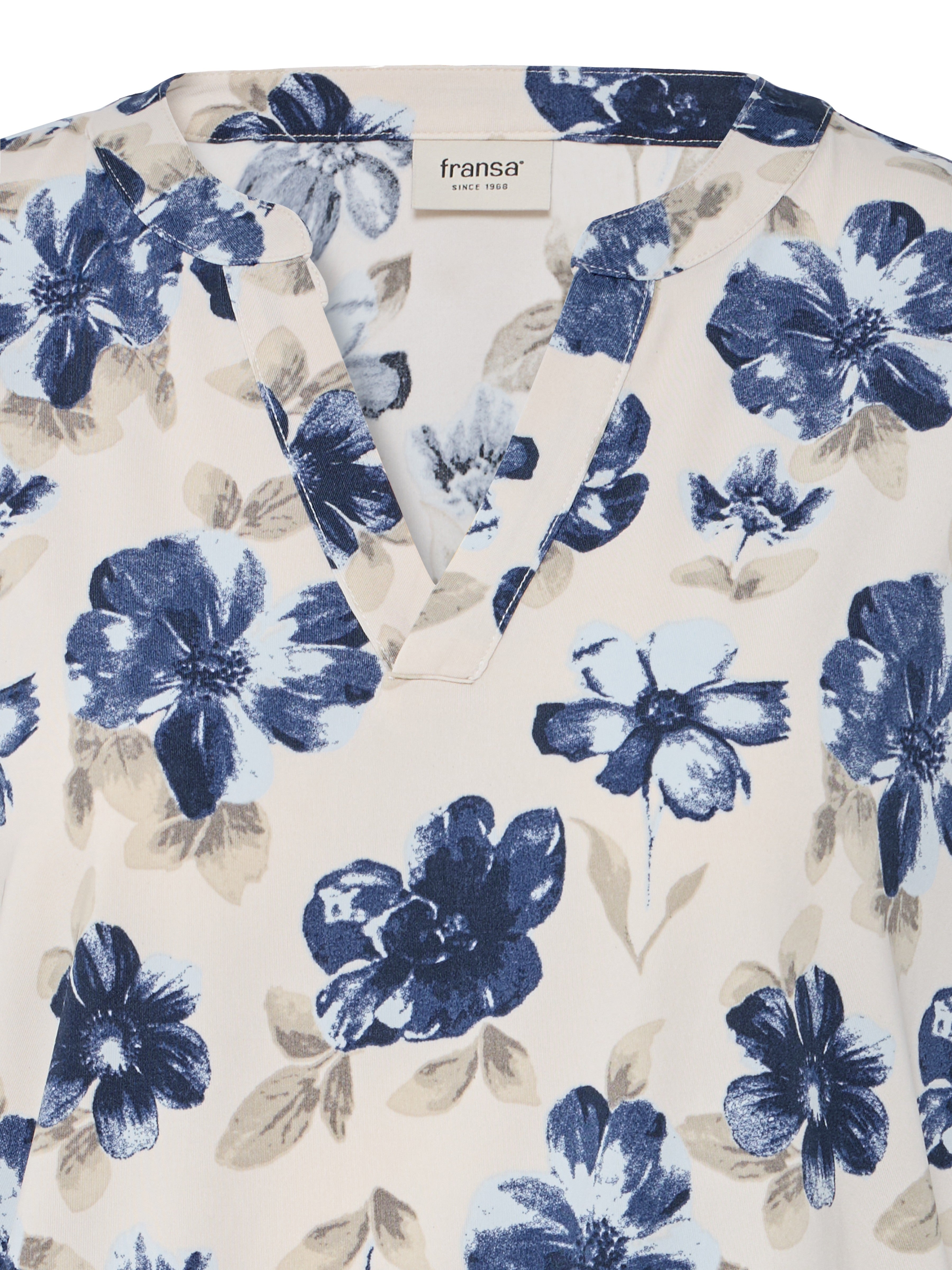 Close-up of beige fabric with blue and tan floral print and V-neck collar with brand label sewn inside neckline