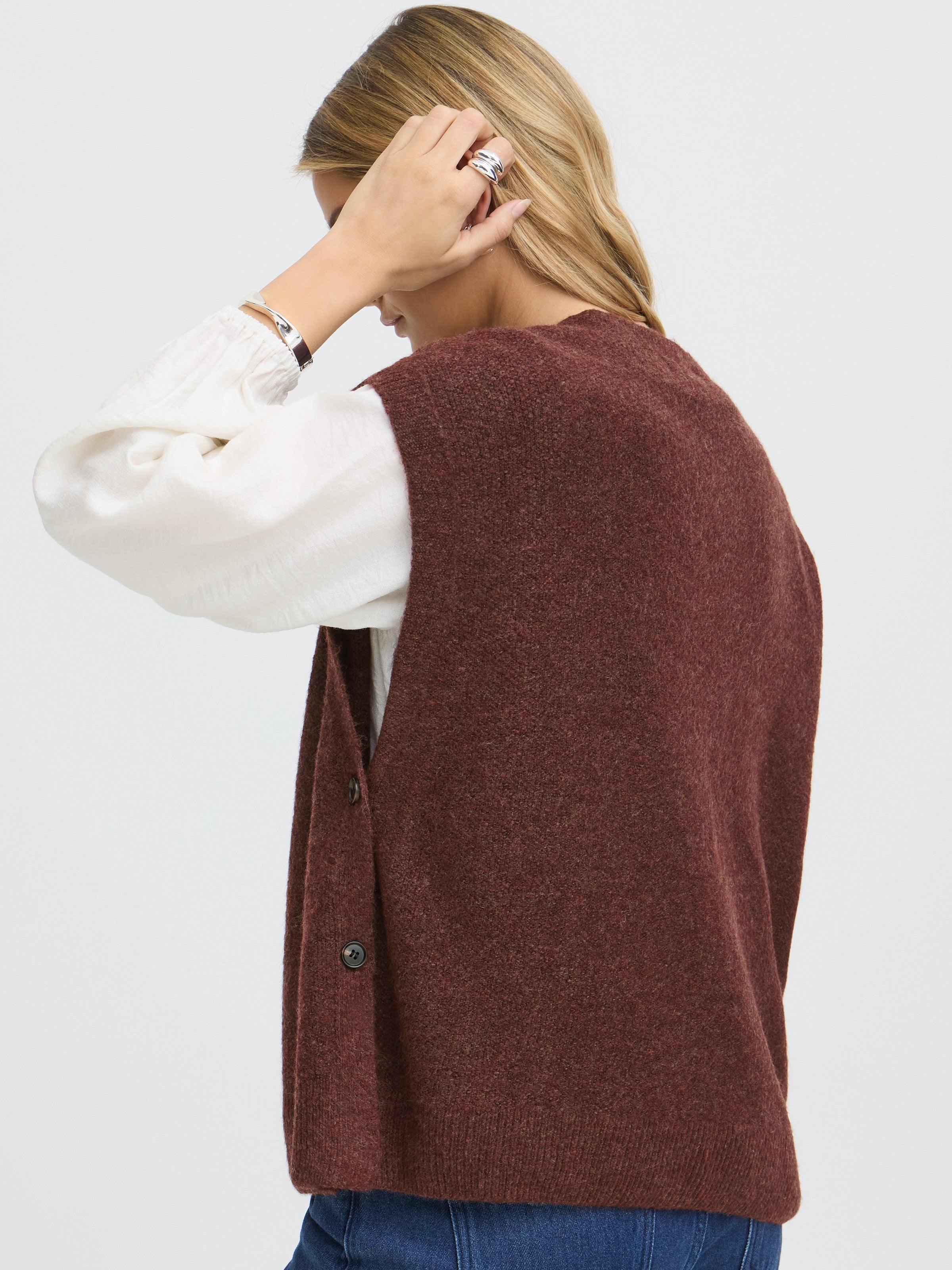 Brown textured knit sleeveless vest layered over a white long-sleeve blouse with button details on the side