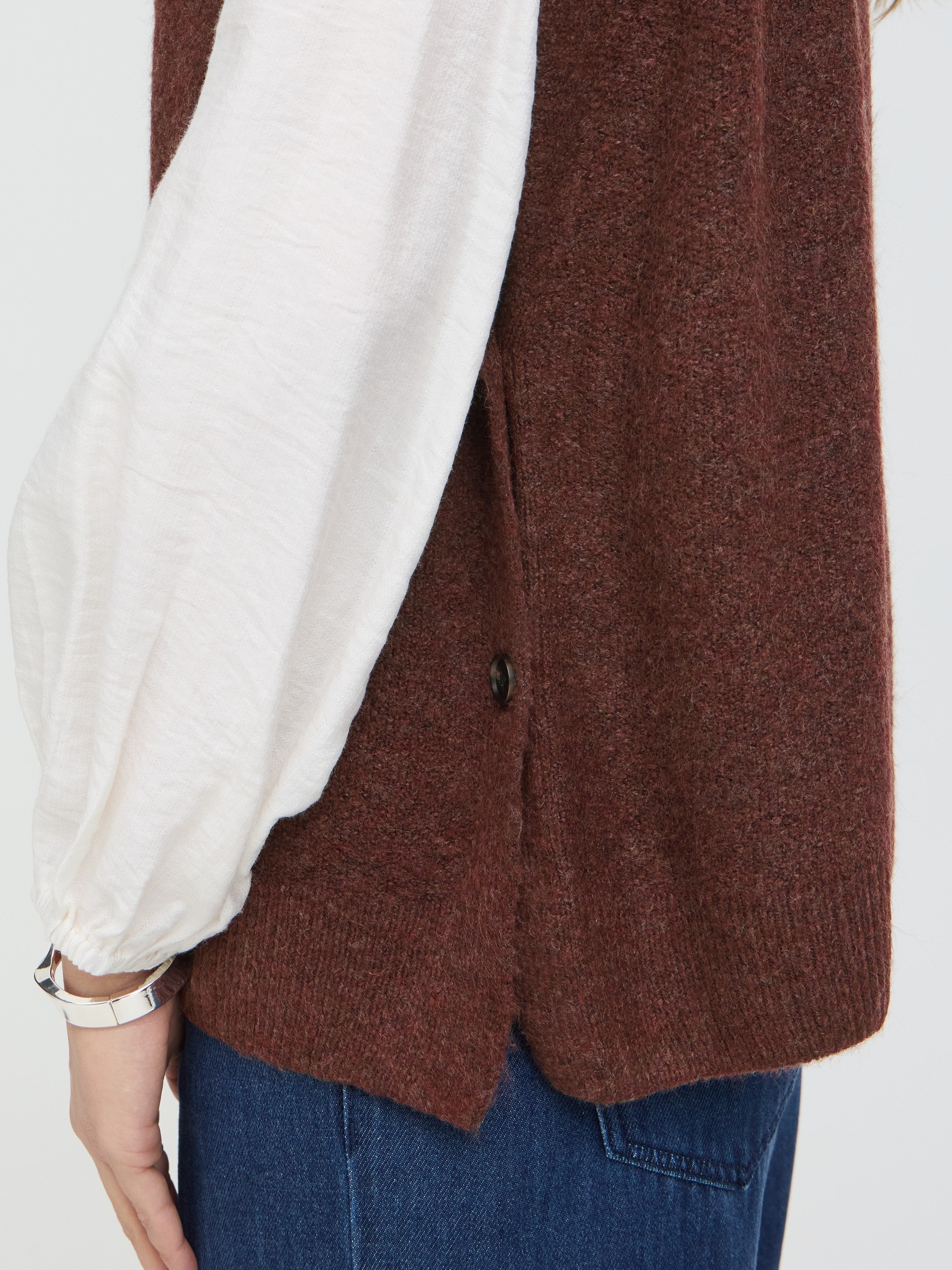 Close-up of a brown woolen sweater layered over a white long-sleeve top with blue denim jeans.