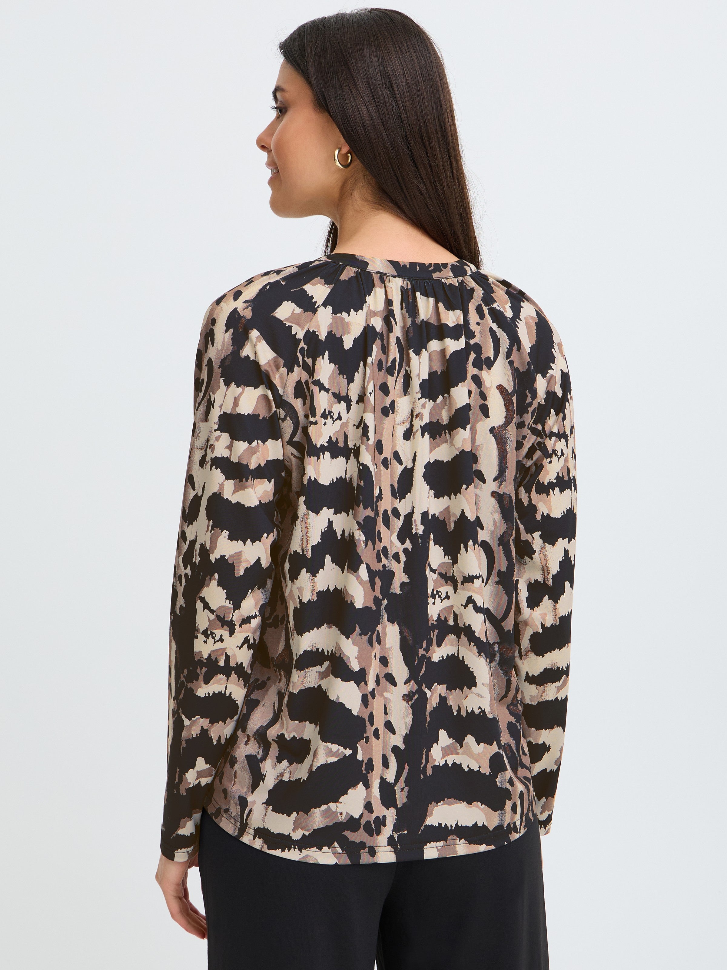 Back view of a long-sleeve top with an abstract animal print in neutral tones and black pants.