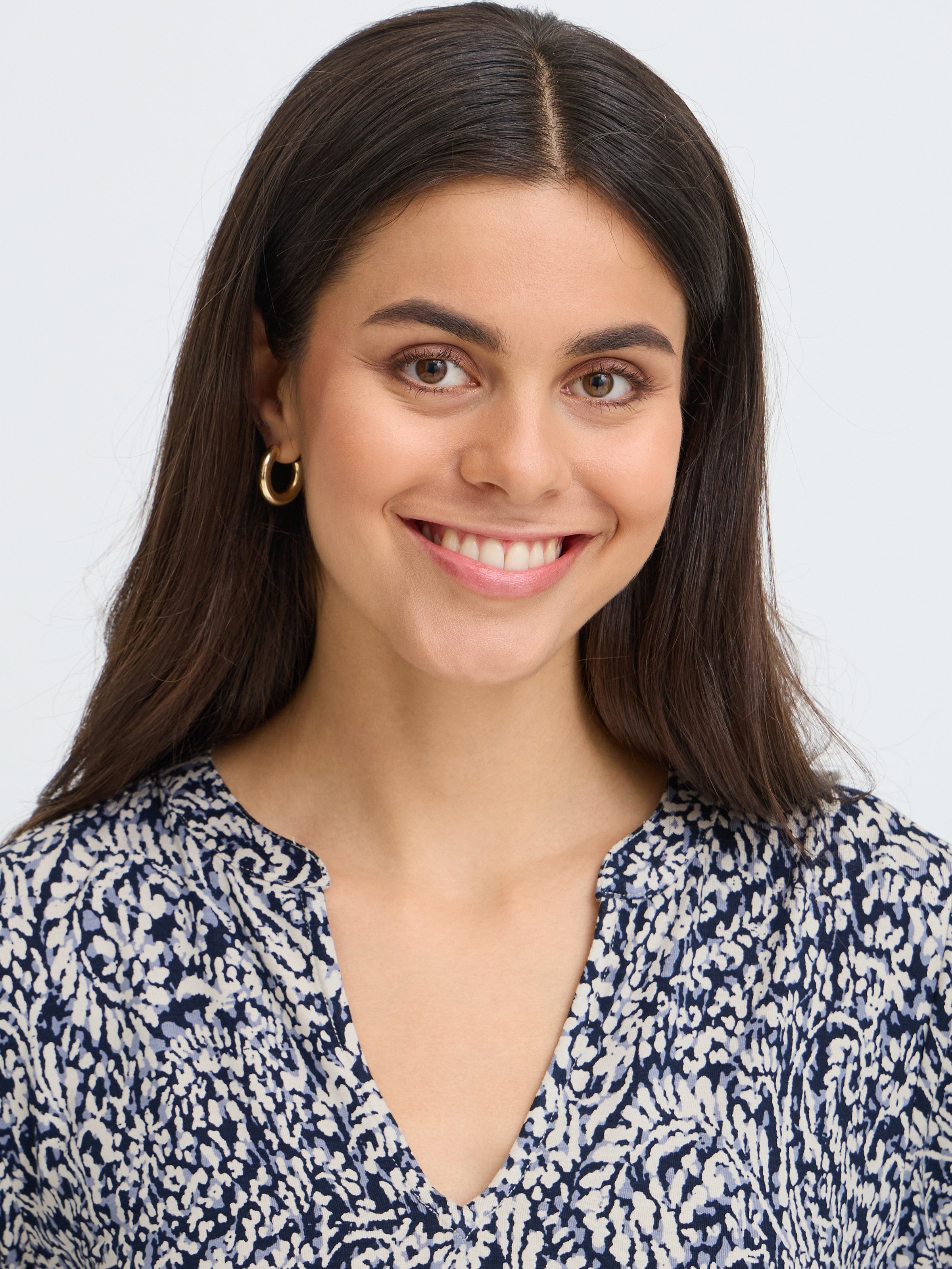 Close-up portrait of an individual with long dark hair, gold hoop earring, and a blue and white patterned top.