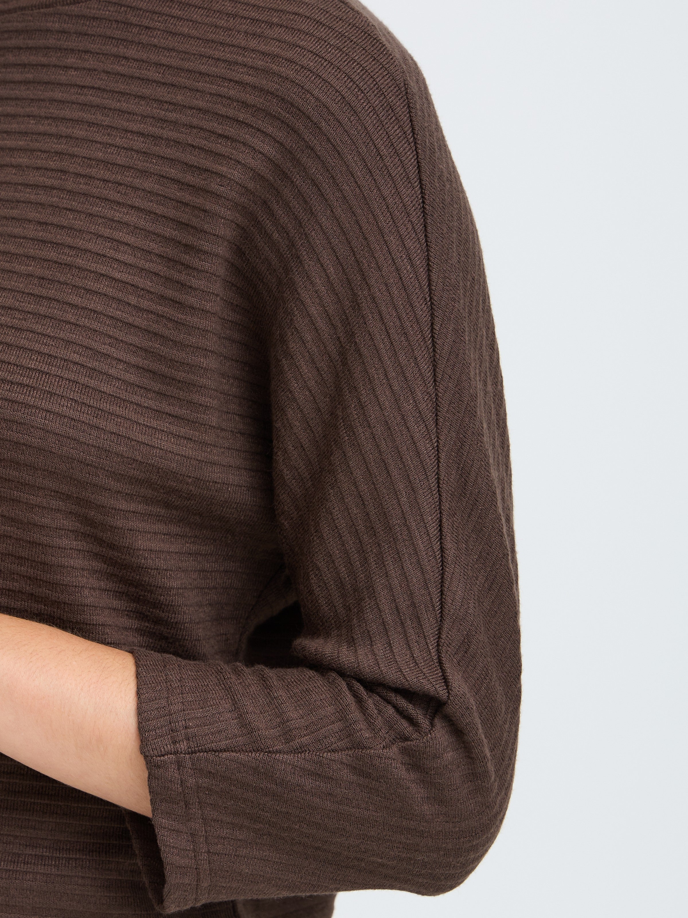 Close-up of a brown ribbed knit sweater sleeve with a visible shoulder seam and cuff detail.