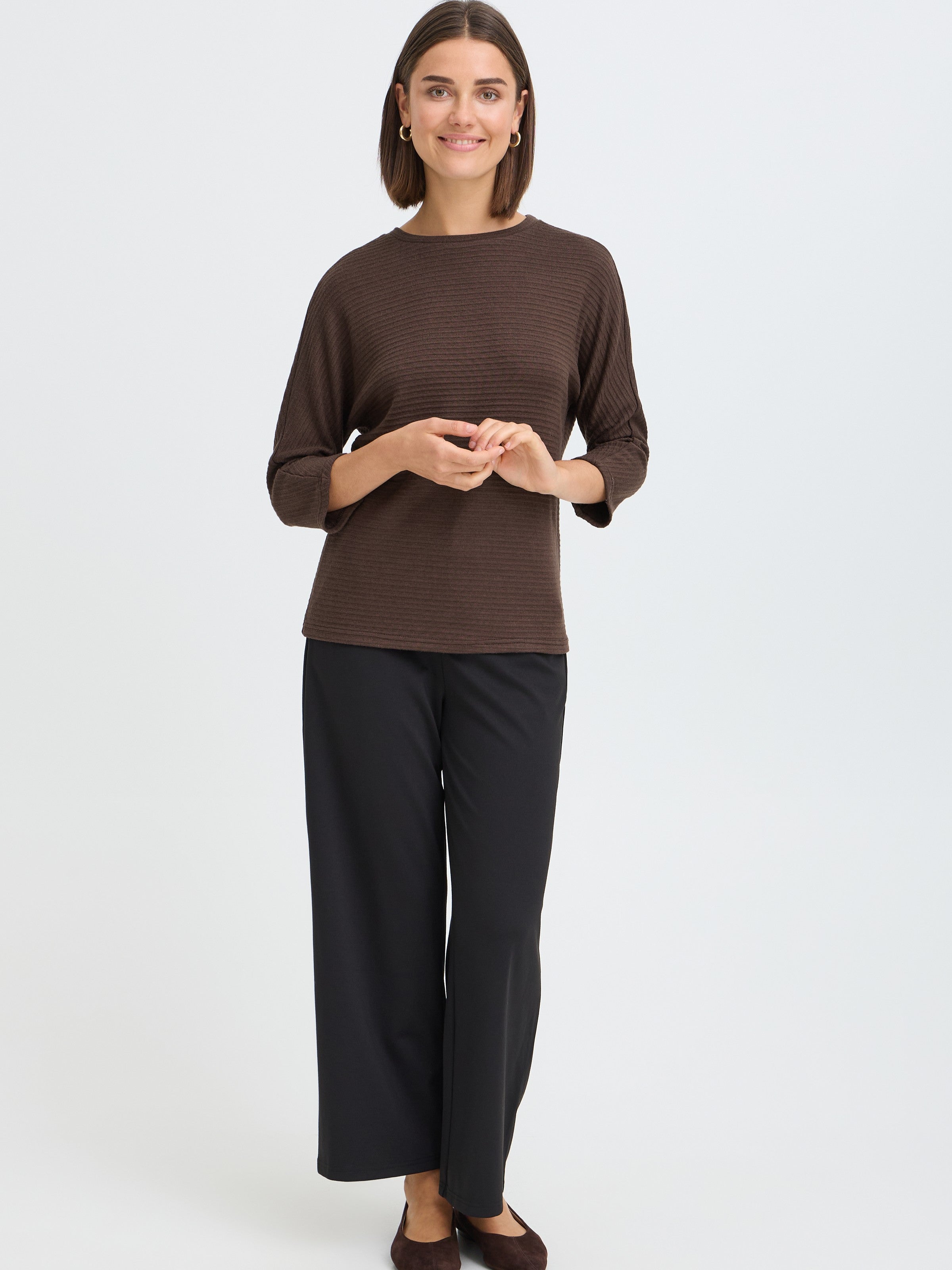 Model in a brown ribbed long-sleeve top and black wide-leg pants standing against a plain background.